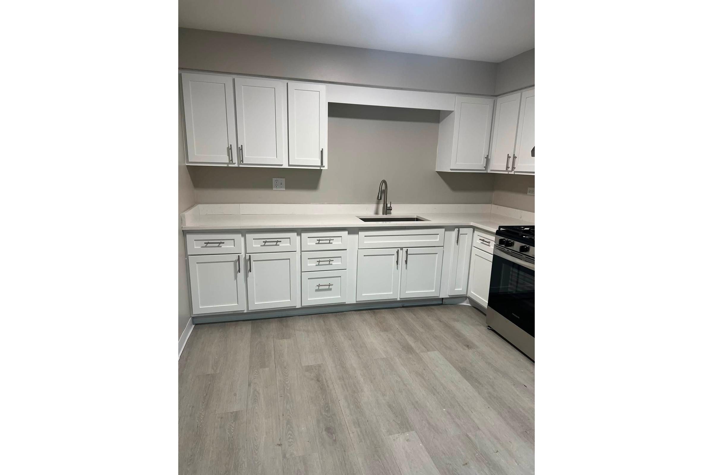Modern kitchen featuring white cabinetry with sleek silver handles, a neutral wall color, a stainless steel sink, and a stovetop range. The flooring is light wood, and the overall design conveys a clean, contemporary aesthetic.