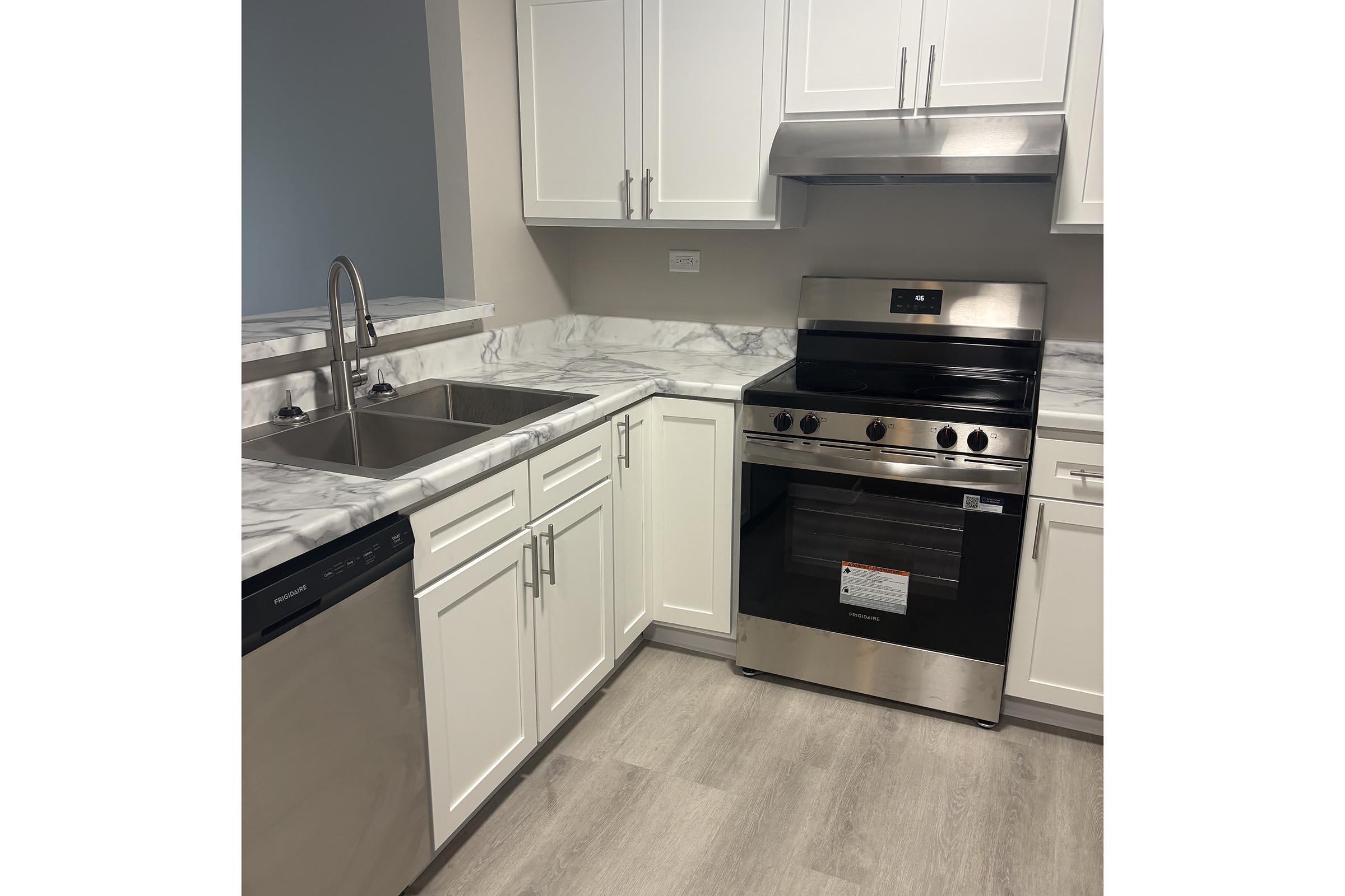 Modern kitchen featuring white cabinetry, a stainless steel stove, a double sink, and a sleek countertop with a marble design. The floor is light-colored, and appliances are in good condition, creating a clean and contemporary look.
