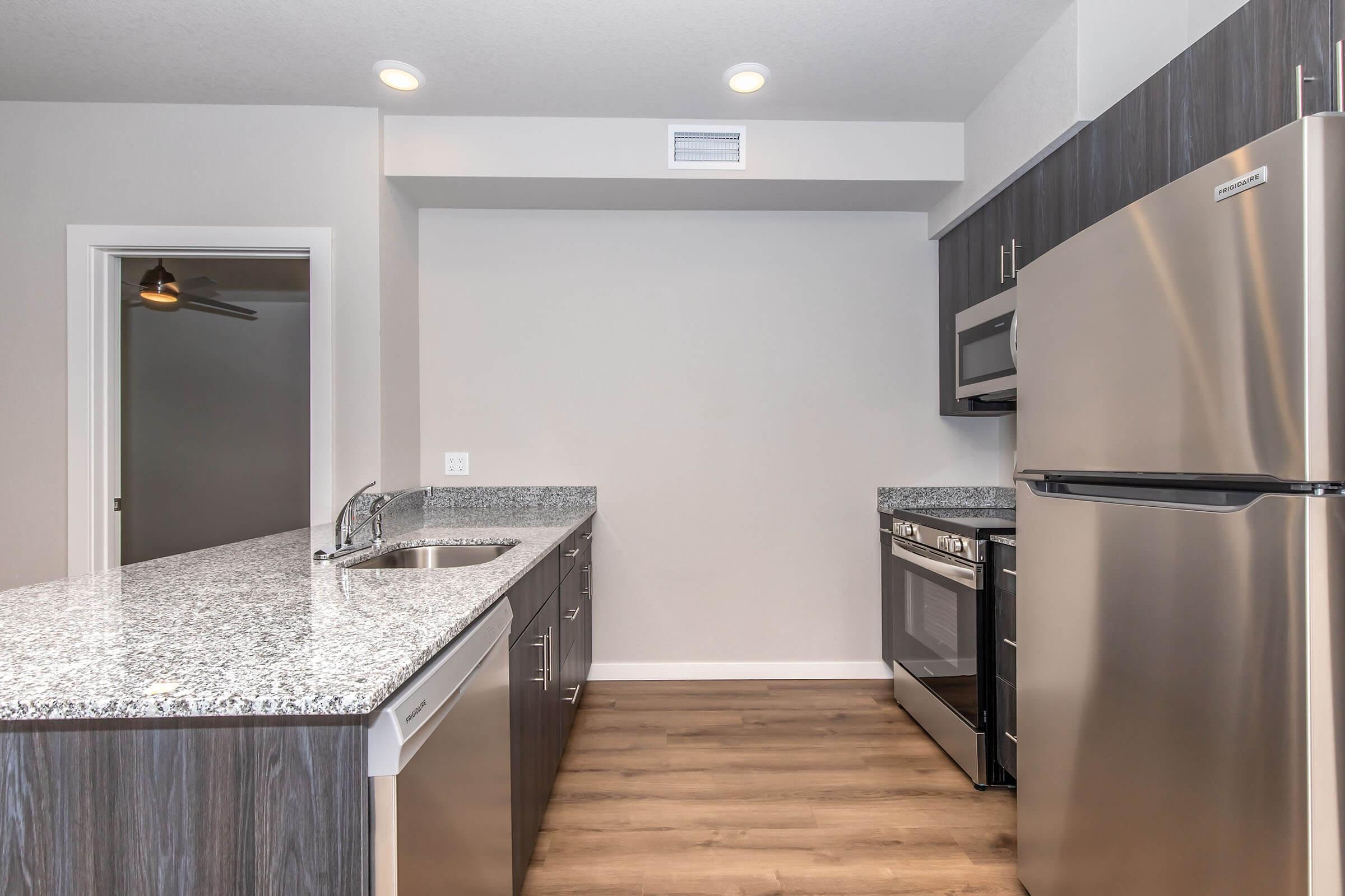 Modern kitchen featuring a sleek design with dark cabinetry, stainless steel appliances including a refrigerator and microwave, and a granite countertop. The space has ample natural light and an open layout, highlighting a blend of functionality and style.
