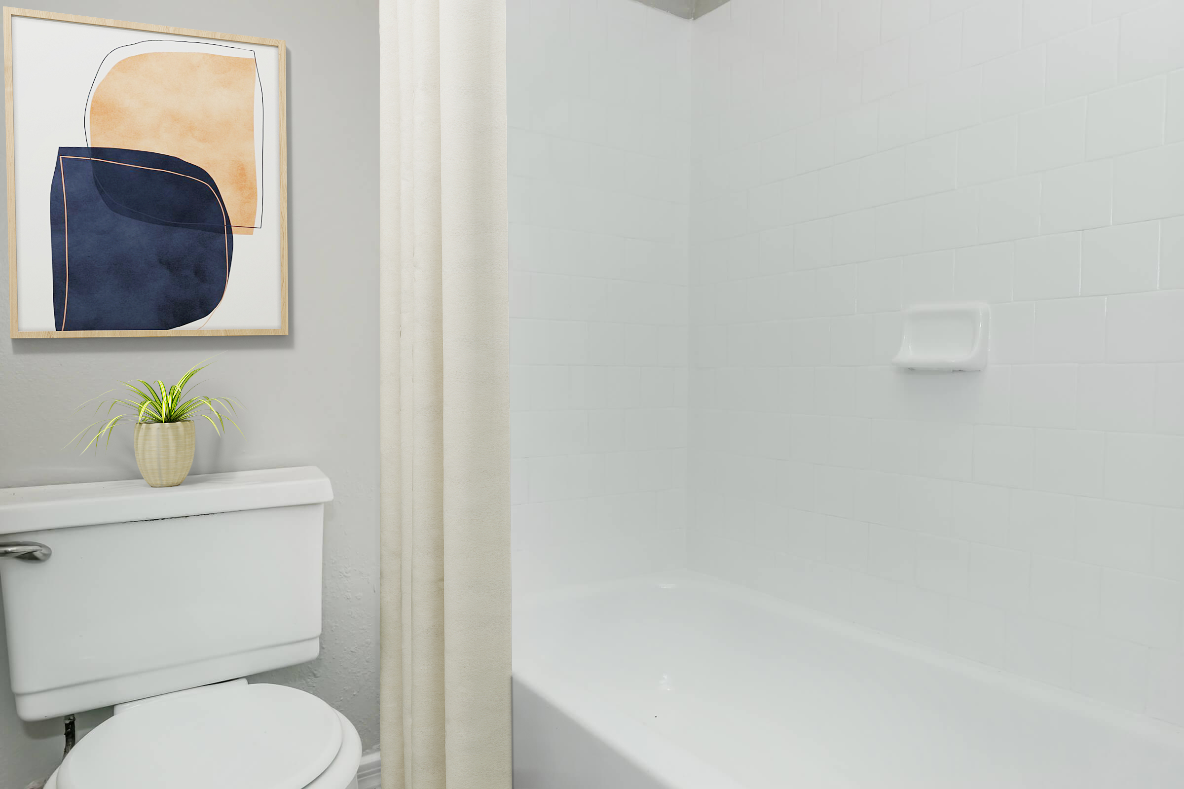 A clean bathroom featuring a white bathtub and shower area, a modern toilet, and a neutral wall color. Above the toilet, there is a framed abstract art piece with geometric shapes in orange and navy blue. A small potted plant is placed on the toilet tank, adding a touch of greenery to the space.