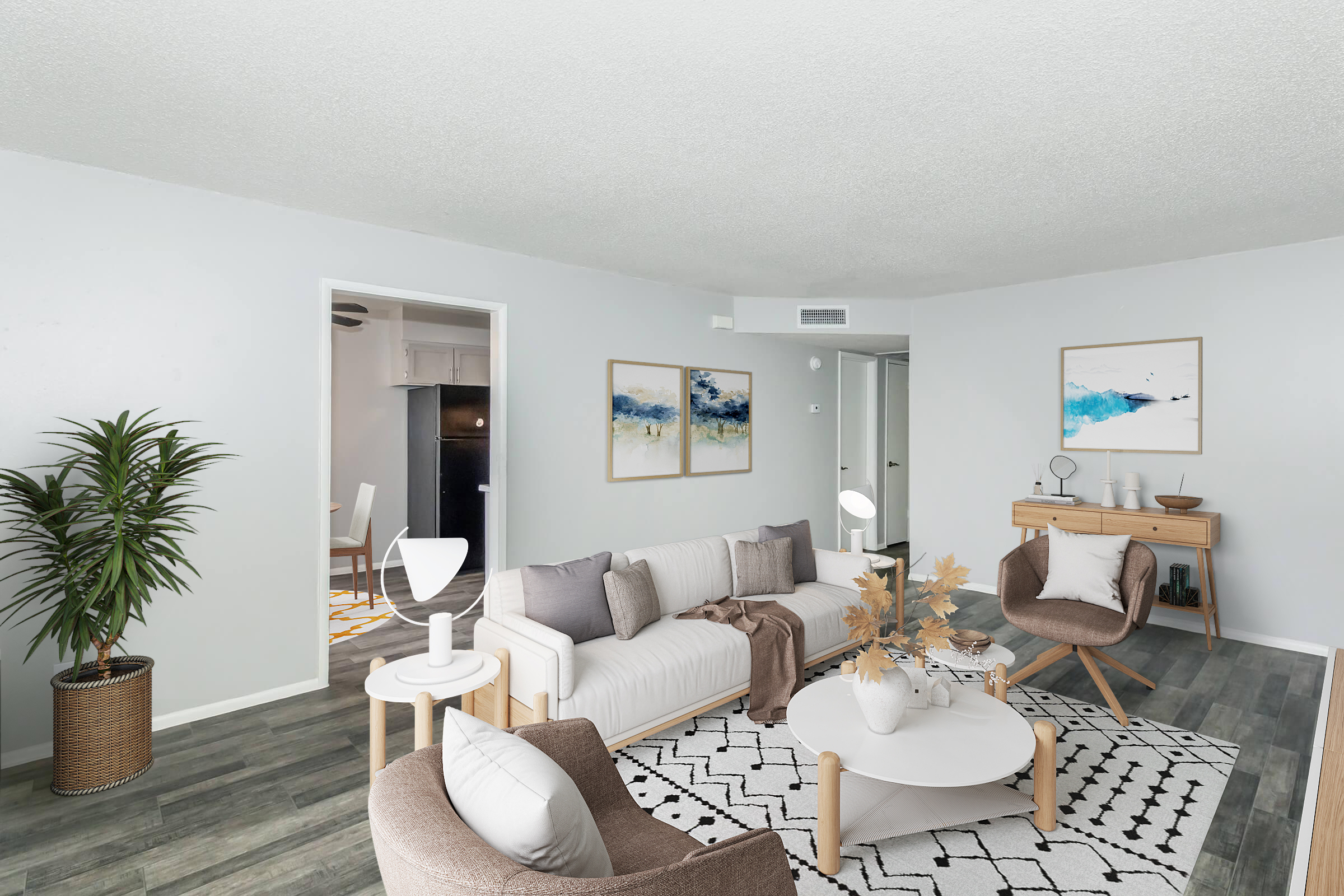 A modern living room featuring light gray walls, a comfortable sectional sofa with decorative pillows, a stylish coffee table, and two accent chairs. Decor includes a potted plant, a minimalist lamp, and abstract art on the walls. A hallway leads to a kitchen area, creating an open and inviting space.