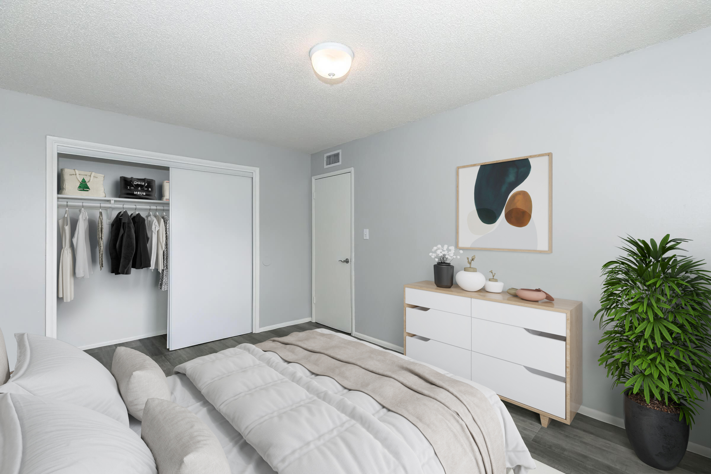A modern bedroom featuring a neatly made bed with soft linens and decorative pillows. A stylish dresser with plants and decor items is against the wall, and a closet with clothes is visible to one side. The walls are painted light gray, and a simple abstract artwork hangs above the dresser. Natural light brightens the space.