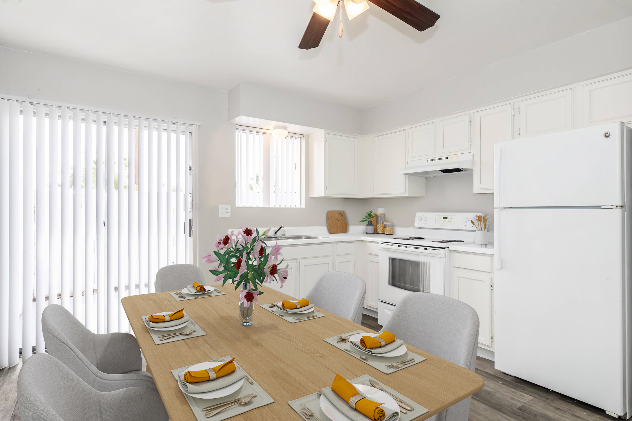 A bright and modern kitchen with white cabinetry and appliances. A dining table is set with neutral plates and yellow napkins, surrounded by light gray chairs. Natural light streams through the window with blinds, creating a welcoming atmosphere. Fresh flowers are displayed in the center of the table.