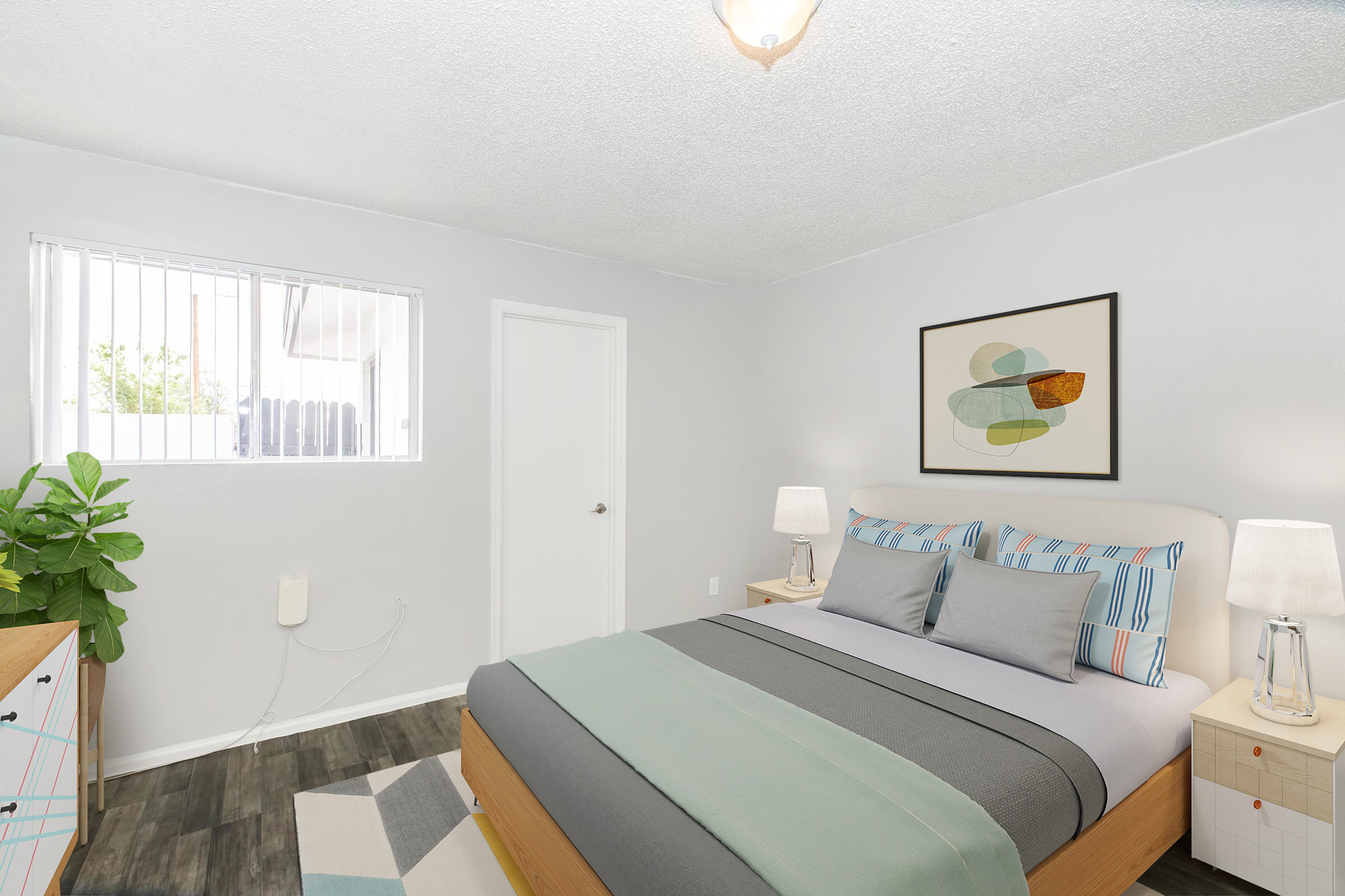 A well-lit bedroom featuring a bed with gray and light blue bedding, flanked by two bedside lamps. There’s a small potted plant in the corner, a framed abstract artwork on the wall, and a light-colored dresser. A white door leads to another room, and a window allows natural light to enter.
