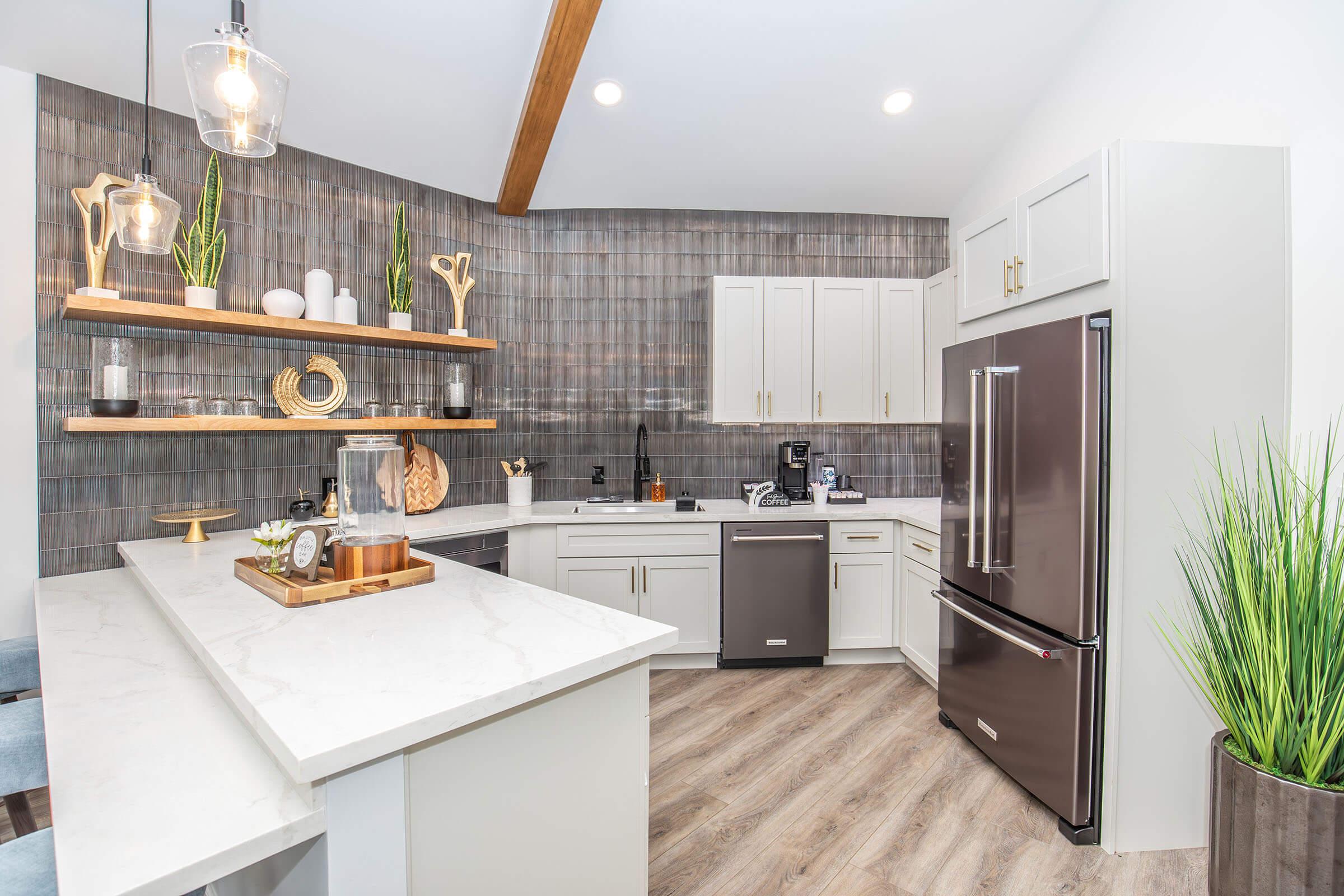 Modern kitchen featuring white cabinetry, a dark stainless steel fridge, and a stylish countertop. Open shelves display decorative items and plants. The room has hardwood flooring and a mix of natural light and stylish fixtures, creating a contemporary and inviting atmosphere.