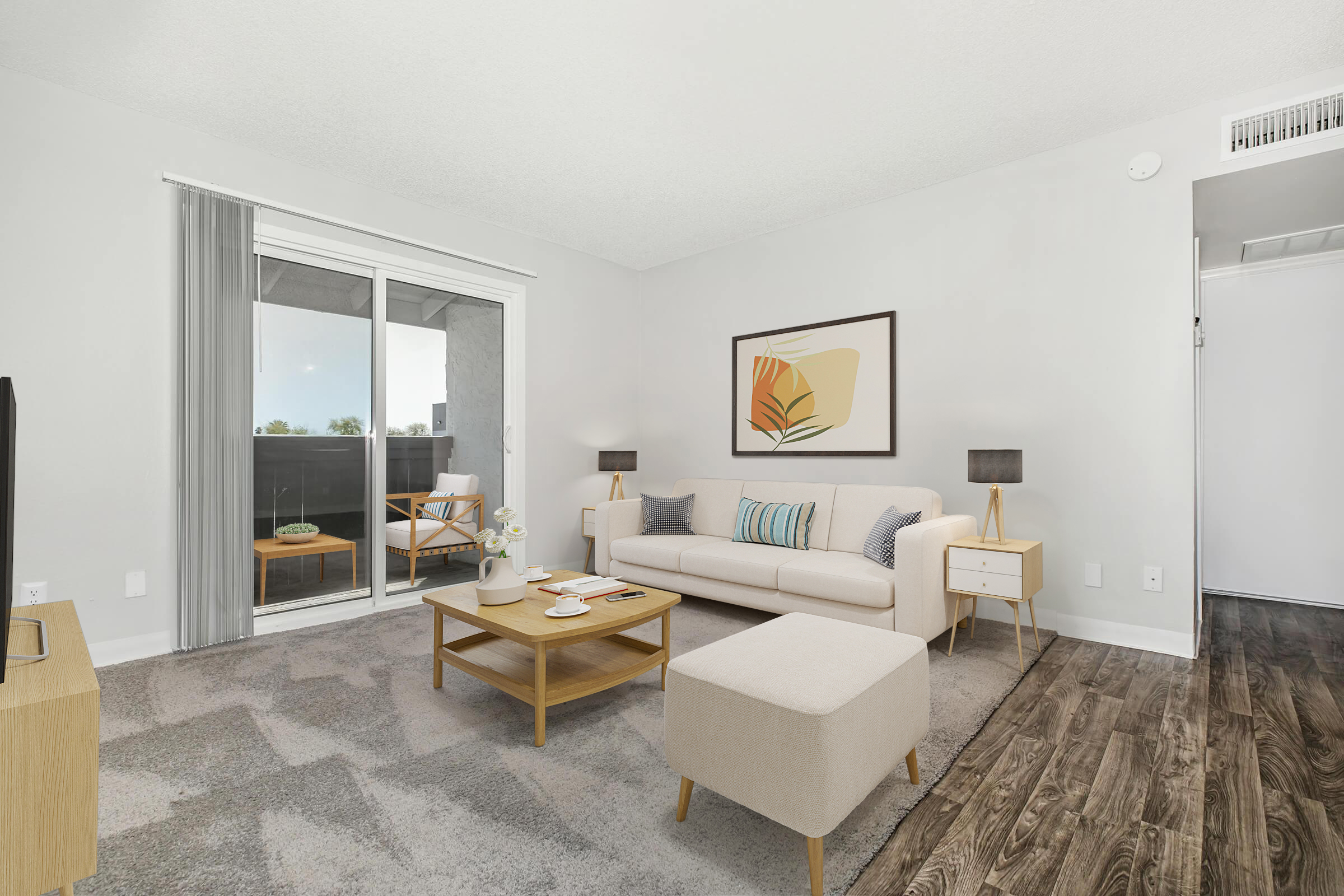 A modern living room featuring a light-colored sofa and matching armchair on a soft rug, a wooden coffee table with decor items, and a wall-mounted television. Large sliding glass doors lead to a balcony, and there are two stylish lamps beside the sofa. Artwork decorates the wall, adding a touch of color.