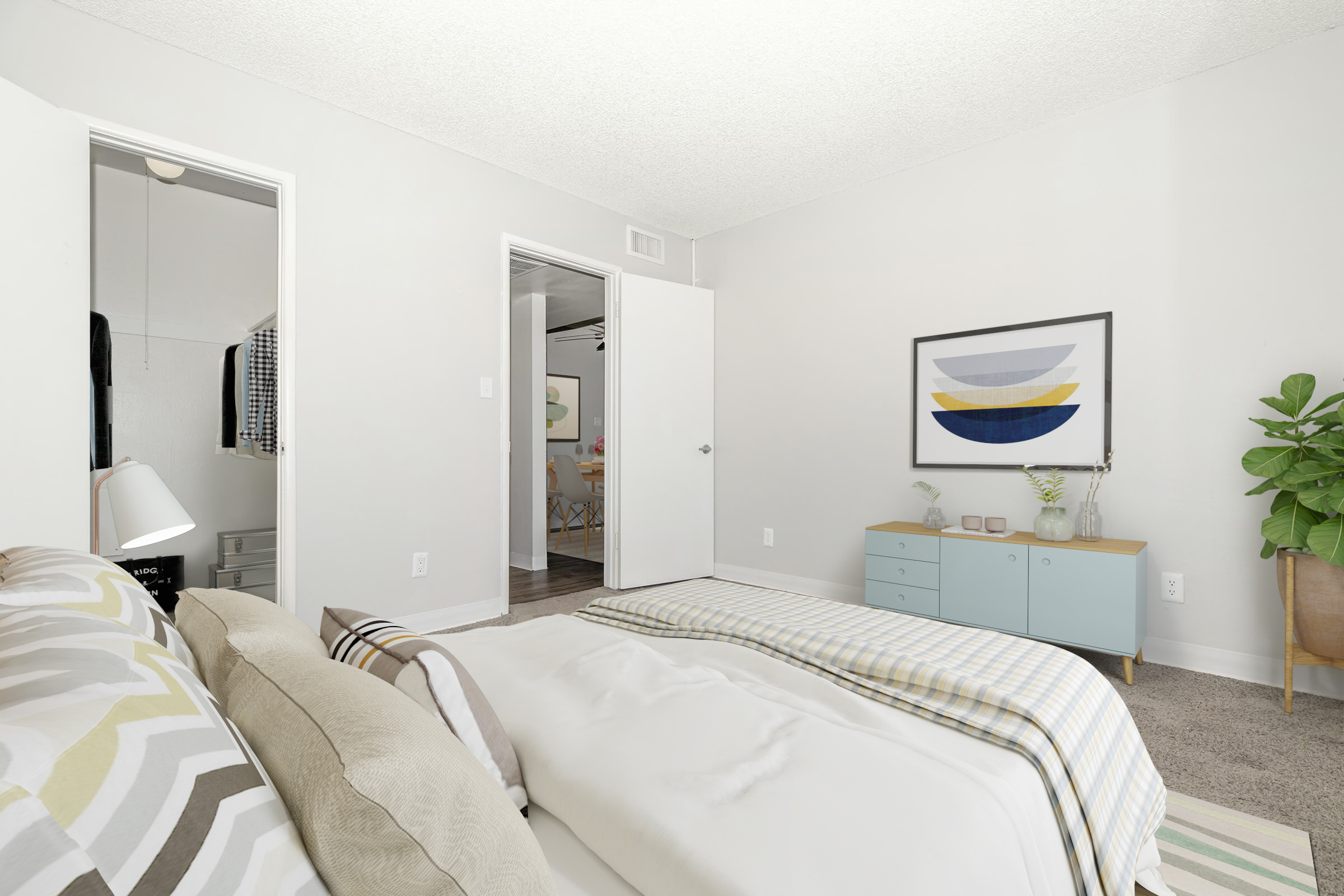 A modern bedroom featuring a cozy bed with striped bedding, a bedside lamp, and a light-colored wall. The room opens to another space, visible through two doorways. A blue dresser sits against the wall, adorned with decorative items, and a potted plant adds a touch of greenery to the decor.