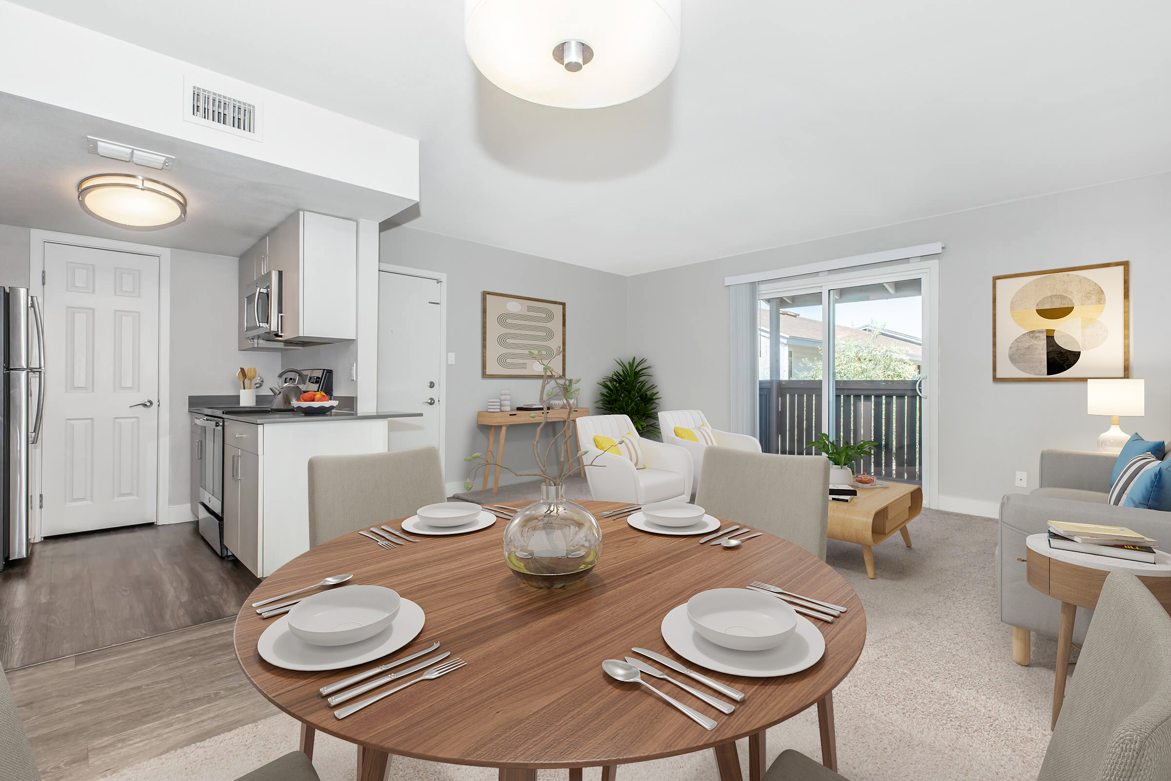 A modern, cozy dining area featuring a round wooden table set with plates and utensils. In the background, there’s a sleek kitchen with stainless steel appliances. The room has soft gray walls and plush seating, illuminated by natural light from large windows. Decorative items enhance the contemporary aesthetic.