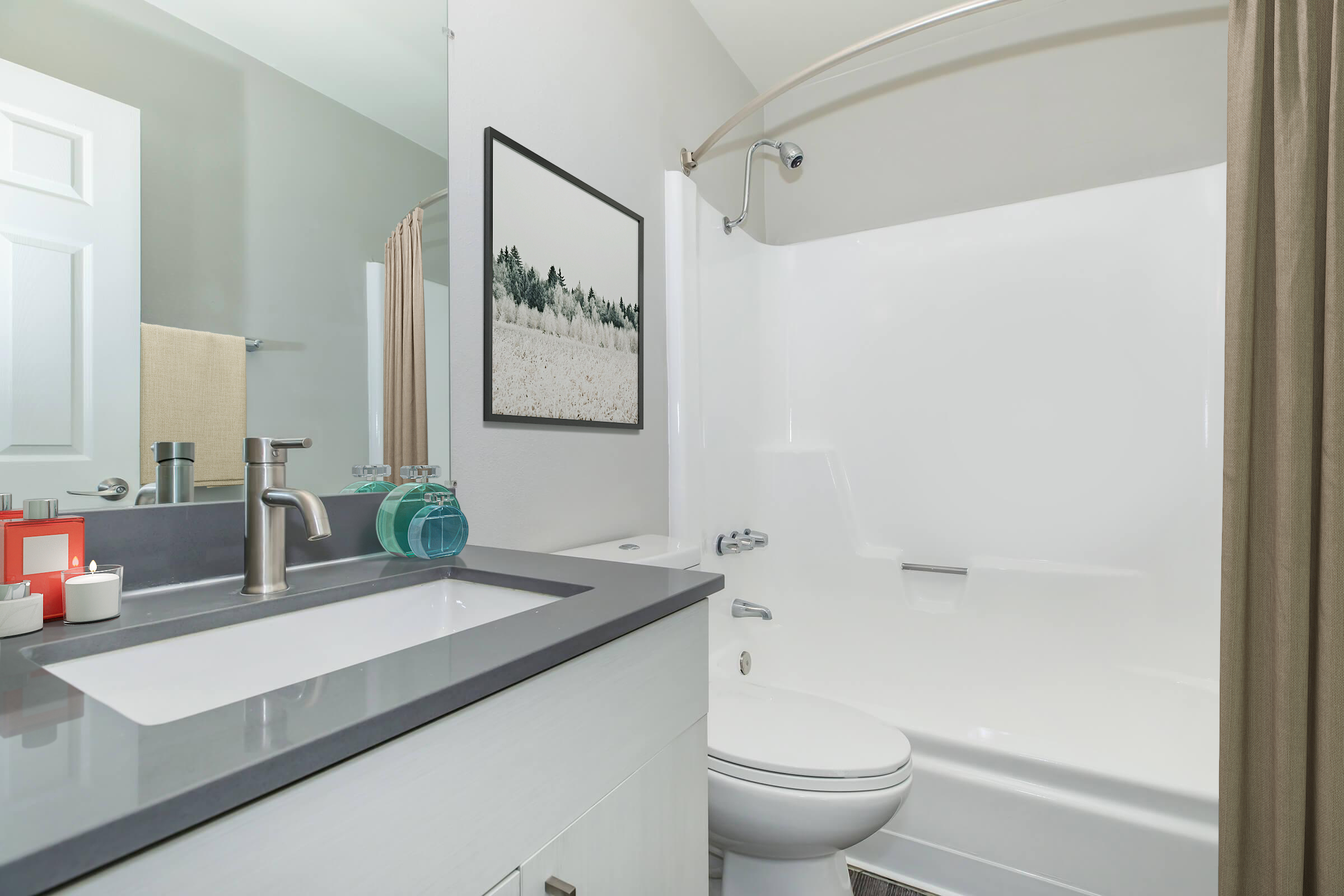 A modern bathroom featuring a white tub and shower, a sleek gray countertop with a sink, a framed picture on the wall, and toiletries neatly arranged. Light-colored walls and a shower curtain create a clean and inviting atmosphere.