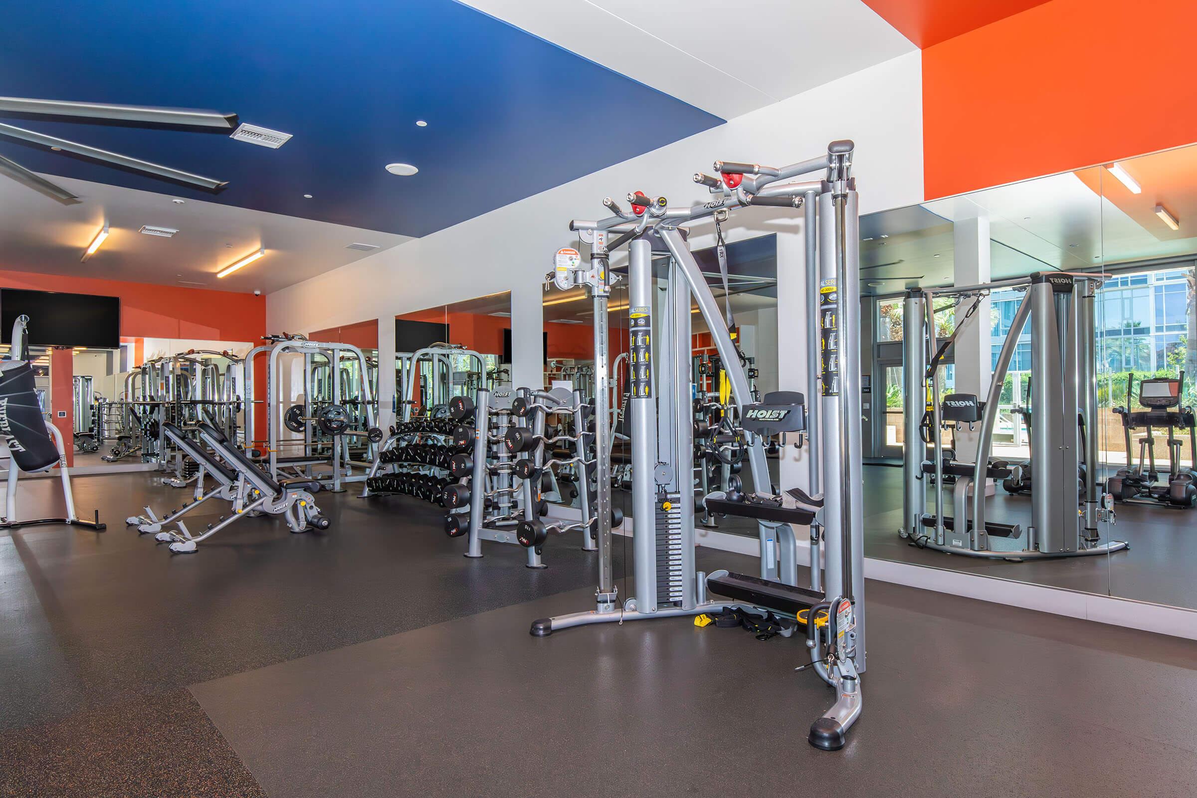 A modern gym interior featuring various exercise equipment, including weight machines, free weights, and cardio machines. The space is brightly lit with large mirrors and colorful walls, creating an inviting atmosphere for workouts.