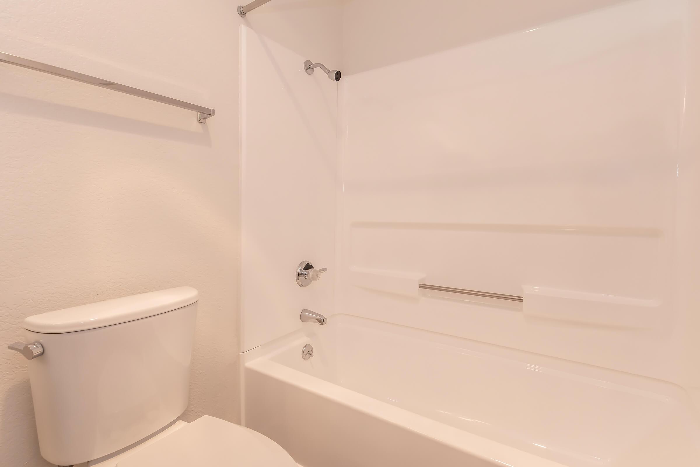 Clean and minimalistic bathroom featuring a white bathtub, toilet, and wall-mounted towel rack. The walls and fixtures are all in light colors, creating a spacious and bright atmosphere.