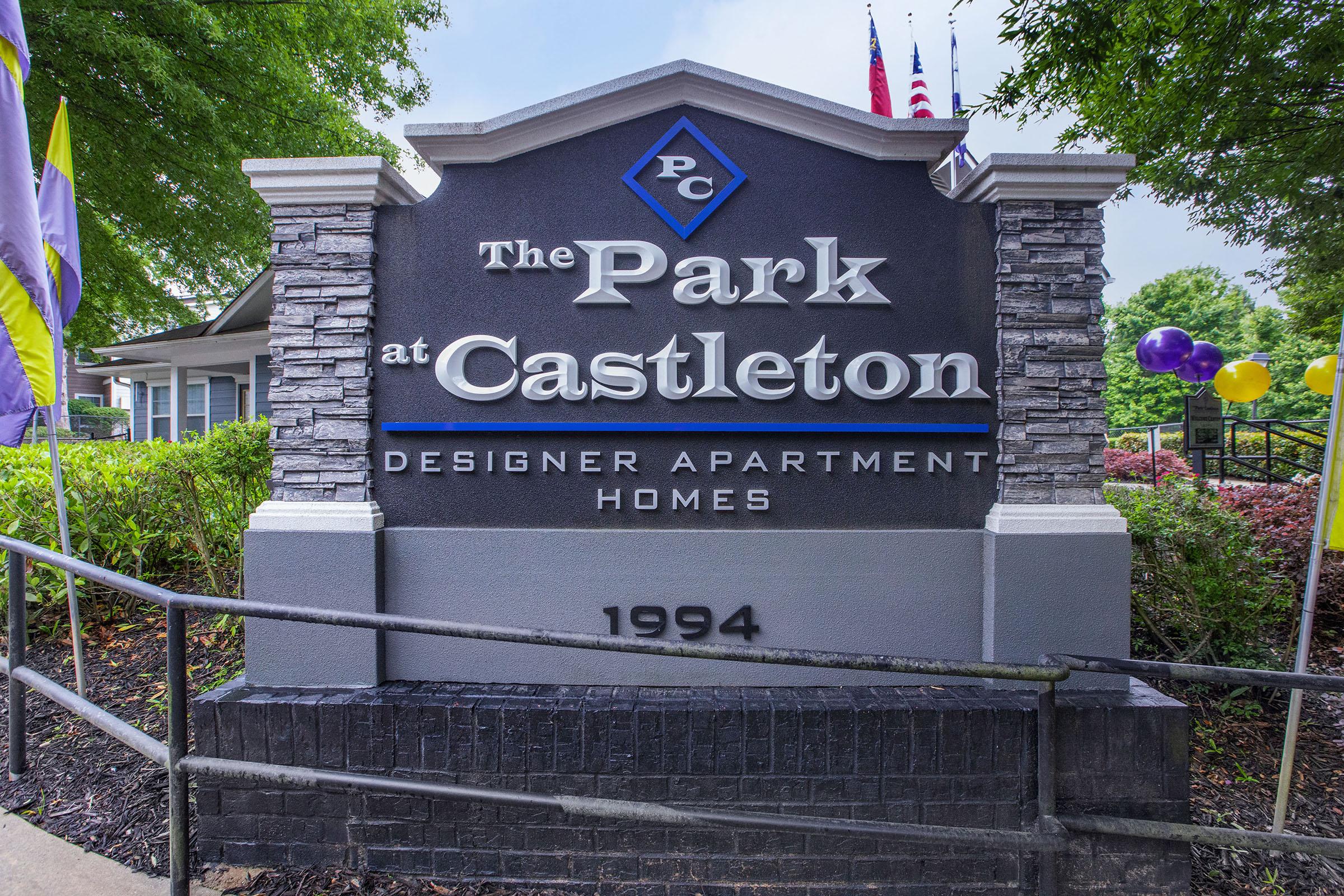 Sign for The Park at Castleton, a designer apartment community. The sign features the year 1994, and is flanked by plants and colorful balloons.