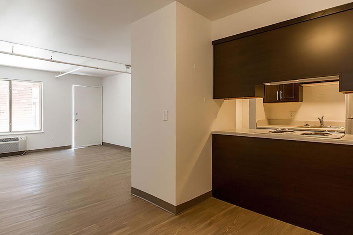 A modern open-concept apartment interior showcasing a kitchen with dark cabinetry and white countertops.