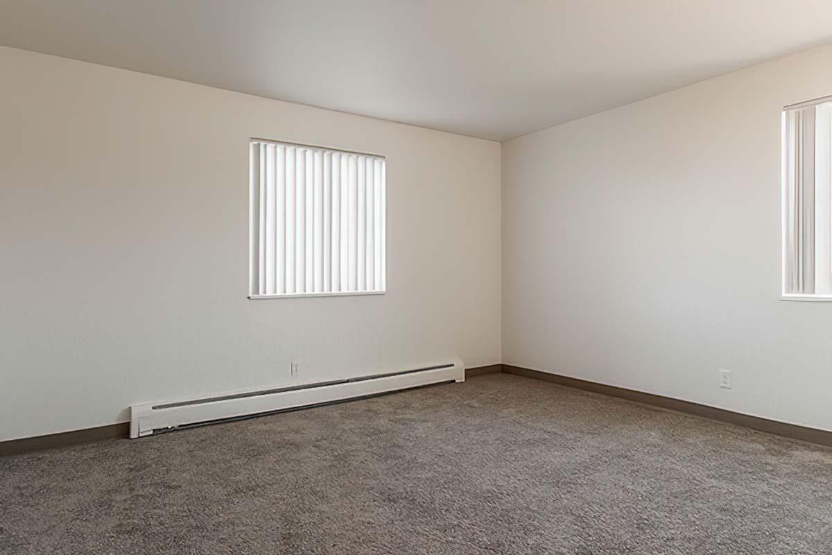 Empty room with pale walls and two windows featuring vertical blinds, illuminated by natural light.