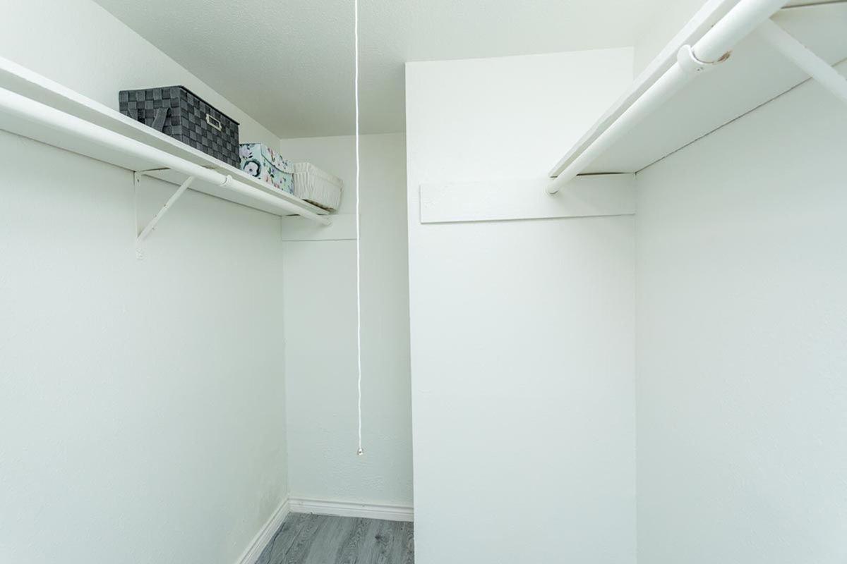 A clean, empty closet featuring white walls and a light gray floor. Two hanging rods are installed for clothing storage, with a few storage boxes neatly placed on top shelves. The overall space is bright and minimalistic, providing a sense of organization and simplicity.