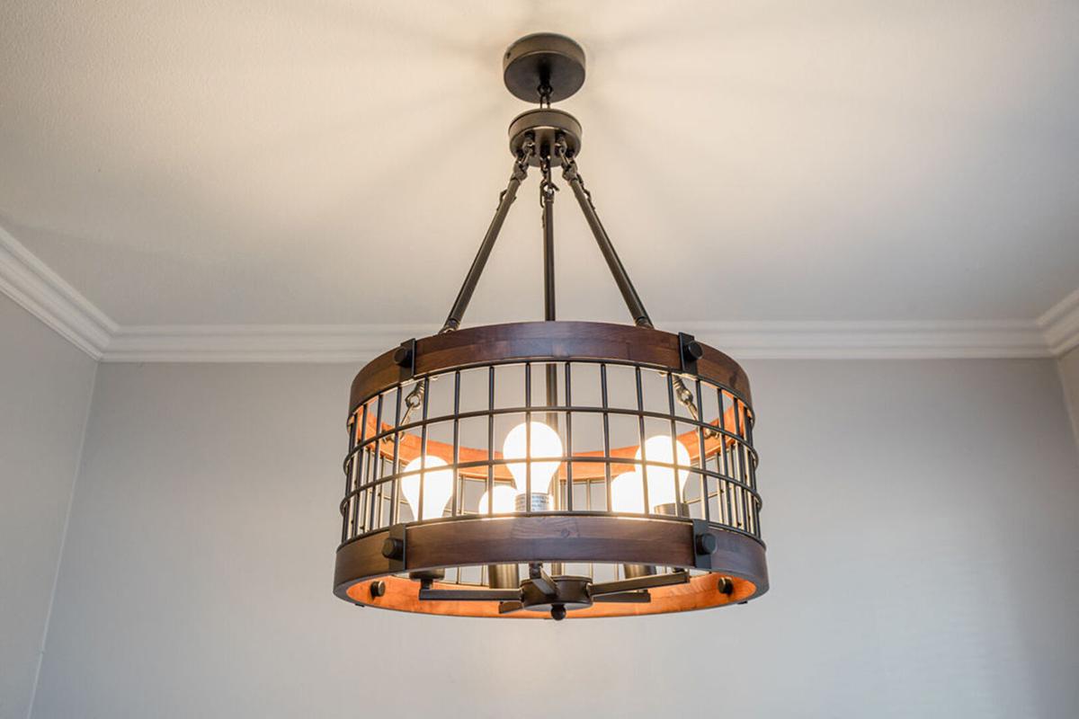 A modern pendant light fixture with a circular metal frame featuring a grid design. It has a bronze finish and houses multiple light bulbs, providing a stylish and warm illumination. The background is a light-colored wall, enhancing the fixture's elegant appearance.