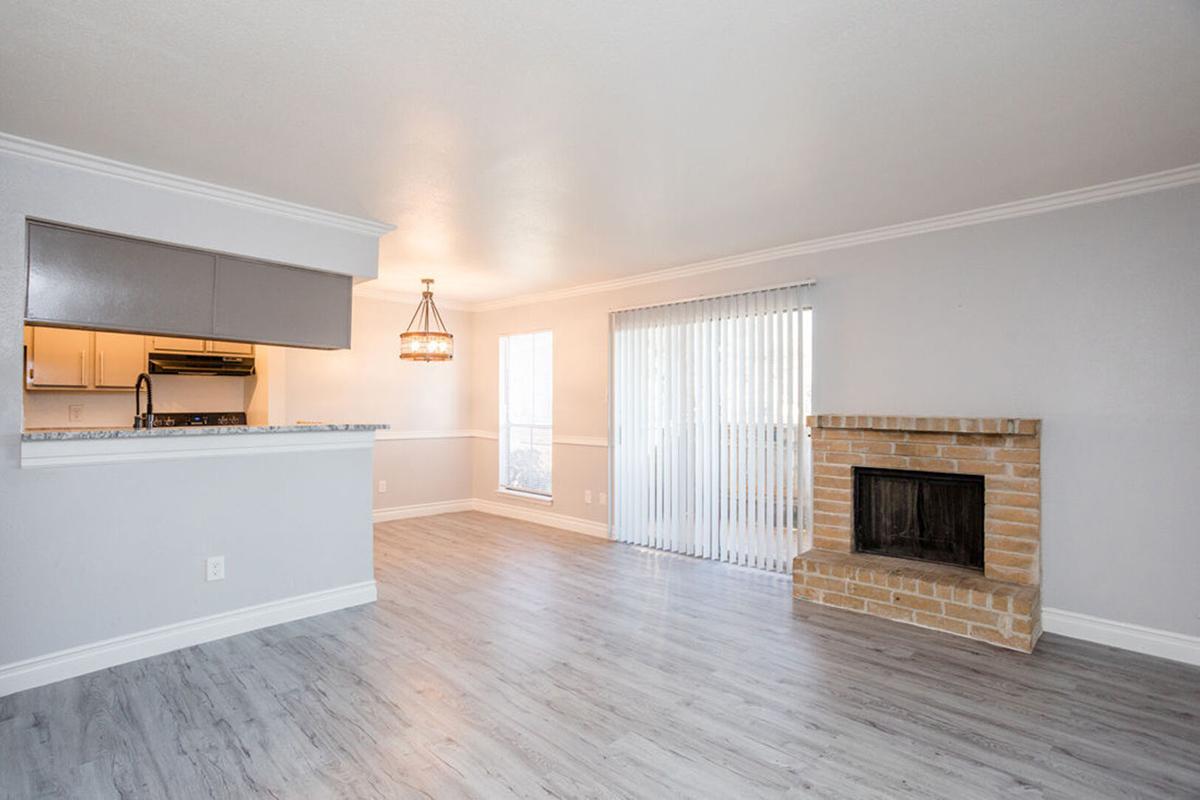 Bright and spacious living area featuring light-colored walls, a modern fireplace made of brick, and large sliding glass doors. The kitchen area is partially visible with sleek cabinetry. Natural light fills the room, enhancing the open and inviting atmosphere of the space.