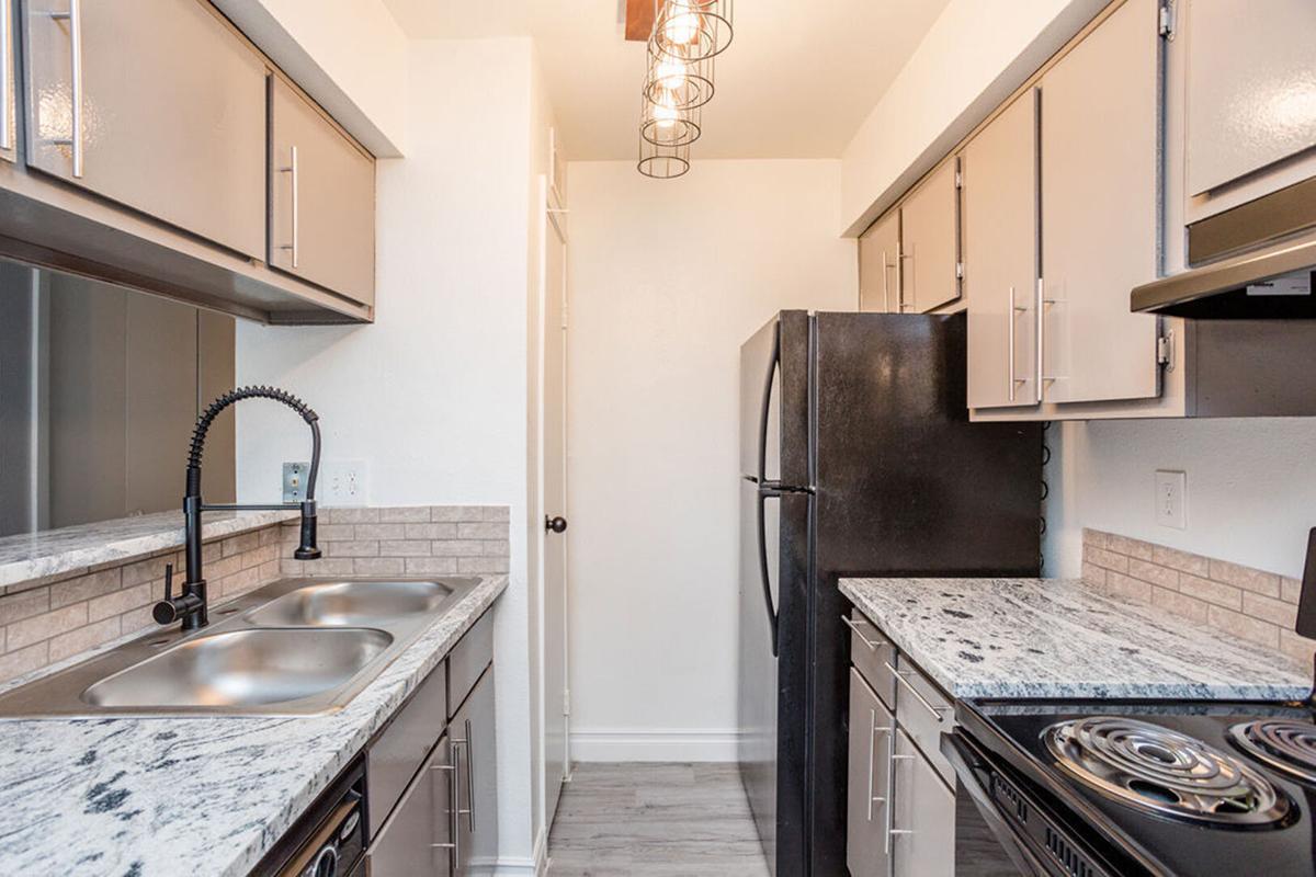 Modern kitchen with light gray cabinets, stainless steel sink, and granite countertops. Features a black refrigerator and stove, with stylish pendant lighting above. The walls are painted white, enhancing the bright and clean ambiance of the space. The flooring is light-colored, contributing to the contemporary look.