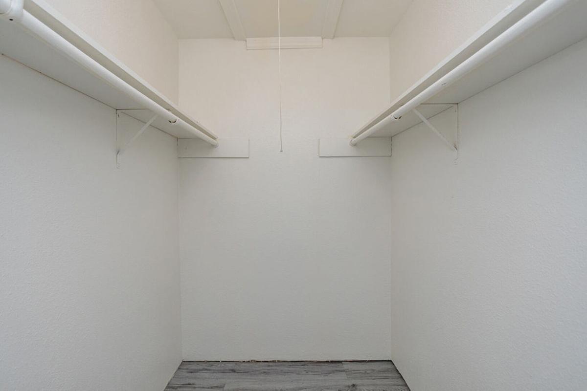A clean, empty closet with white walls and two overhead storage rods. The floor is light-colored, and there are no items or shelving present, creating a spacious and minimalist appearance.