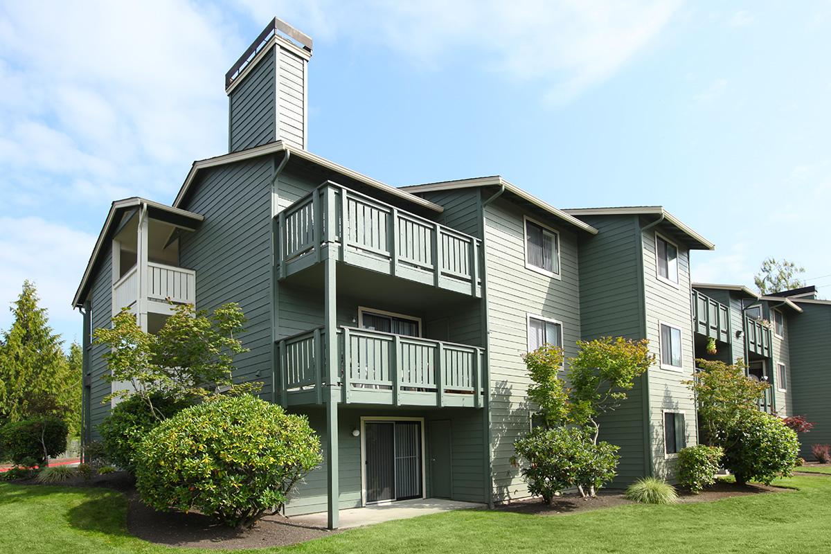 a house with bushes in front of a brick building with Peacefield in the background