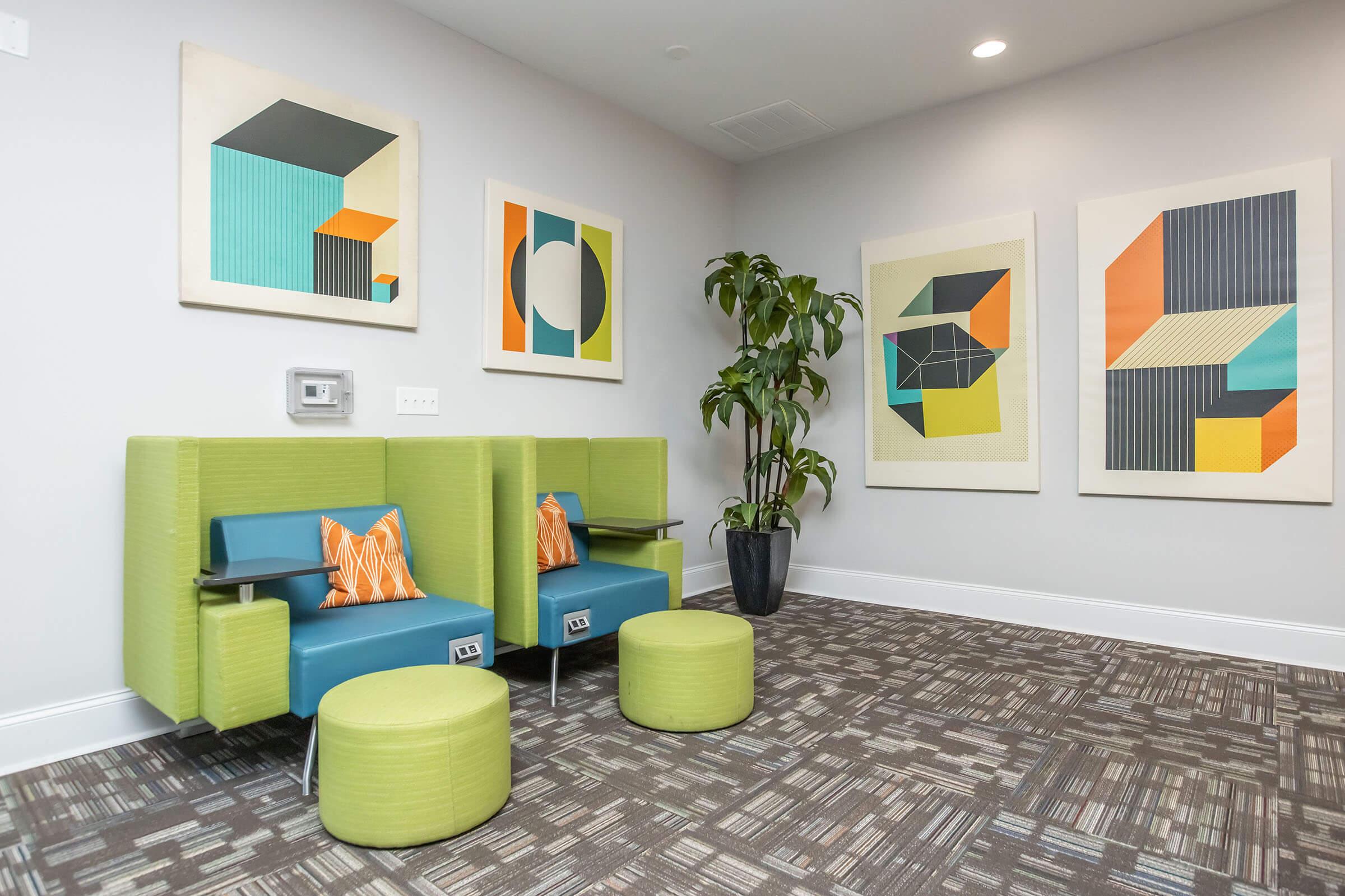 A modern waiting area featuring two green armchairs with orange accent pillows, circular green stools, and contemporary geometric artwork on the walls. A plant is positioned in the corner, and the flooring has a textured pattern. Soft lighting creates a welcoming atmosphere.