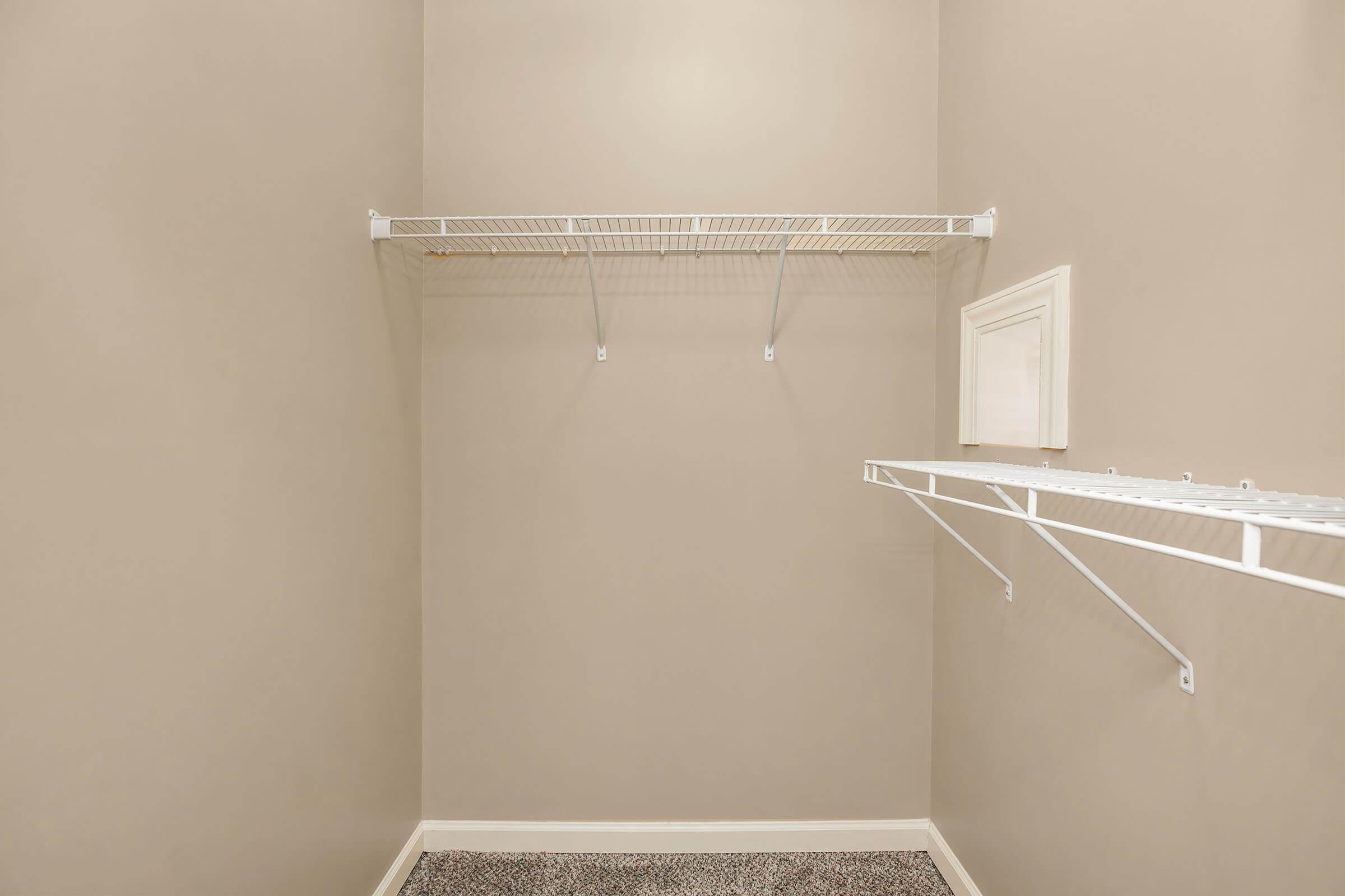 Empty closet with light beige walls and gray carpet. There are two wire shelves mounted on the walls. The space is uncluttered, suggesting it can be used for storage or organization.