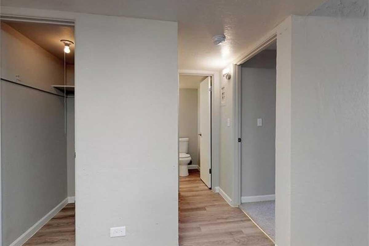 View of an interior space showing a hallway with two doorways—one leading to a bathroom with a toilet and another potentially leading to a closet. The room features light-colored walls and modern wood flooring. A light fixture is visible in the ceiling.
