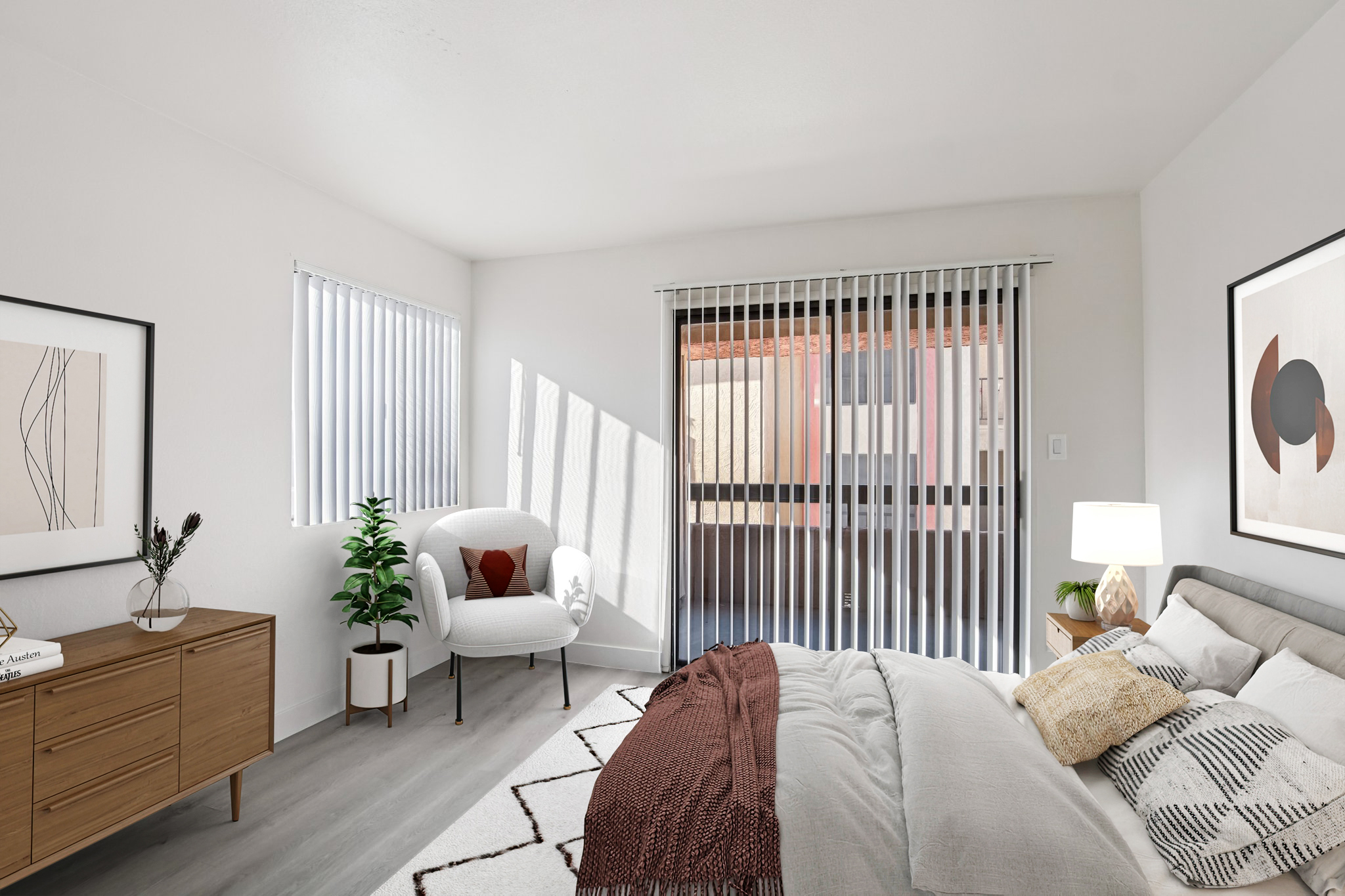 A modern bedroom featuring a cozy bed with light bedding, a stylish armchair next to a potted plant, and a wooden dresser with decorative artwork. Natural light filters through vertical blinds, creating a warm atmosphere, while minimalist decor enhances the space's functionality and aesthetic appeal.