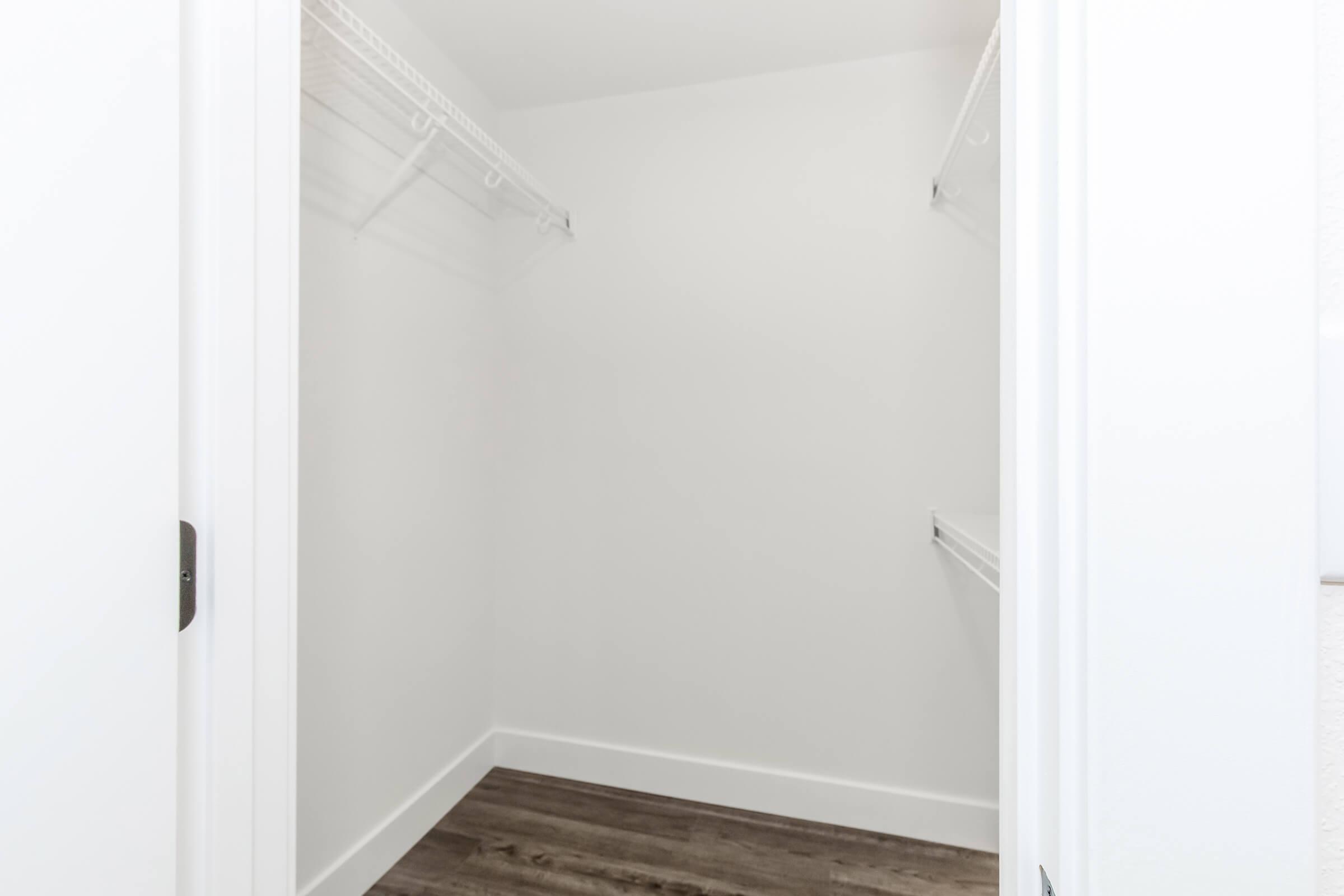 Empty closet with white walls, wooden floor, and wire shelving on two sides. Simple and spacious design, suitable for storage.