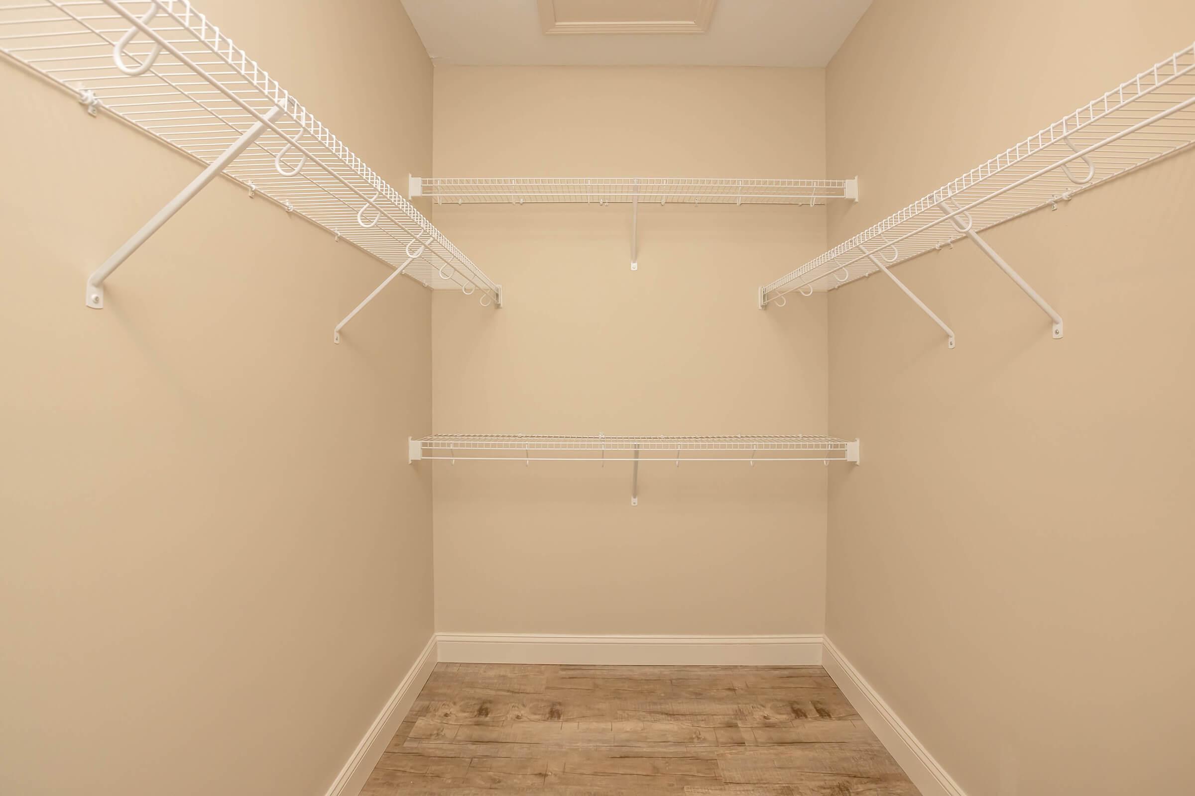 A spacious empty closet featuring white wire shelving. The walls are painted a light beige, and the floor has a wood-like finish, creating a clean and organized appearance.