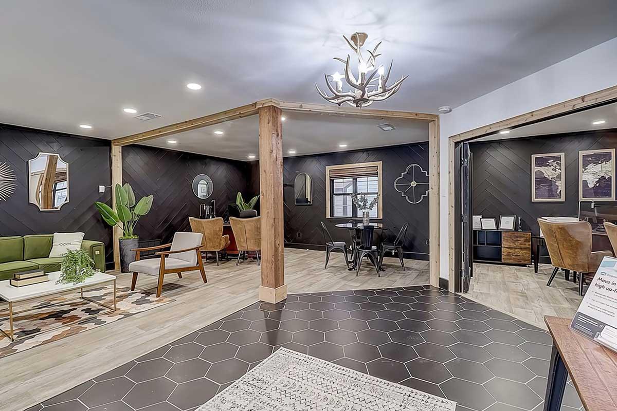 A modern interior space featuring a cozy seating area with a green sofa, wooden furniture, and decorative plants. The room has a stylish black and white color scheme, hexagonal tile flooring, and unique wall art, creating a welcoming and contemporary atmosphere for both relaxation and social gatherings.