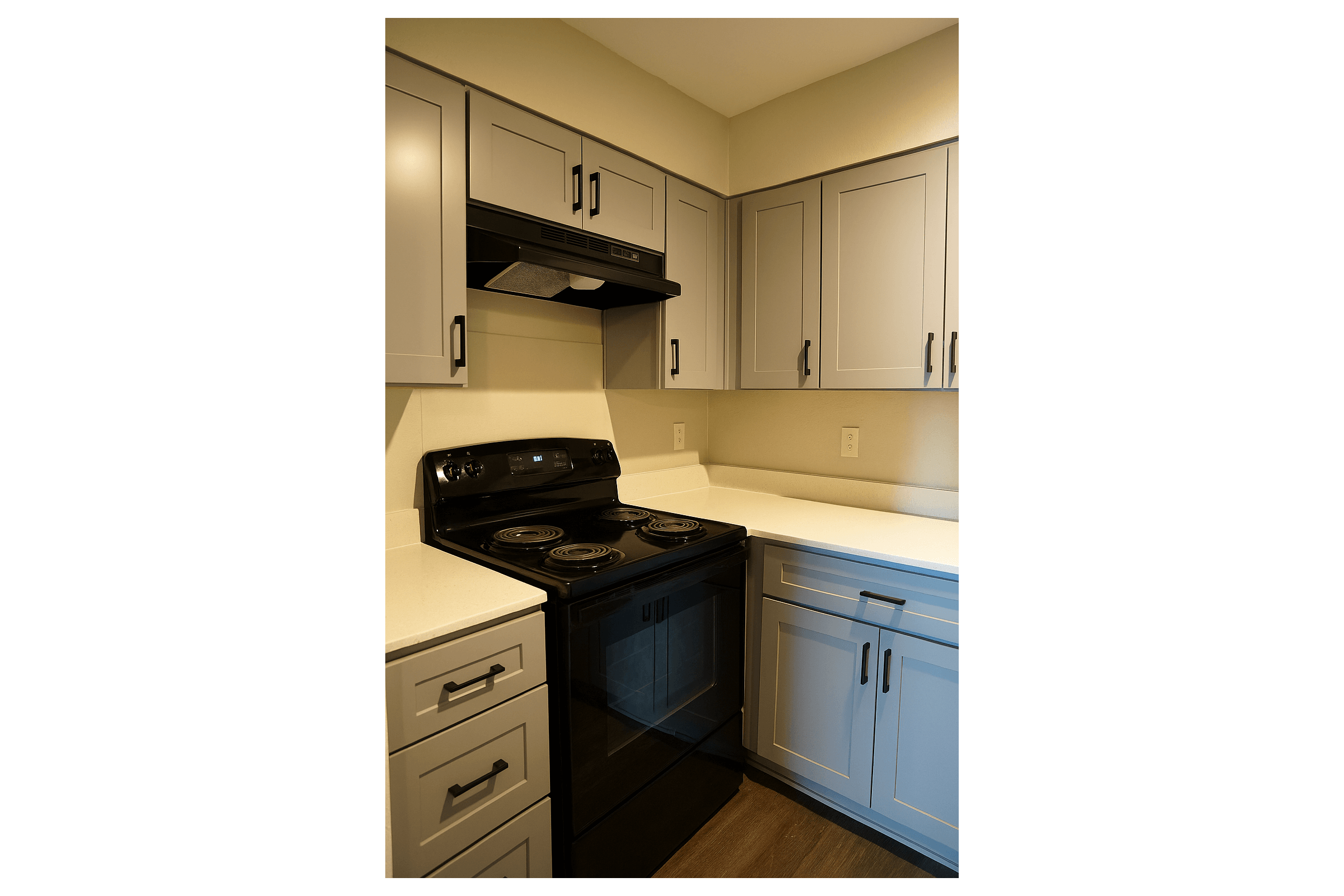 Modern kitchen featuring gray cabinetry, a black stove and hood, and a white countertop. The design highlights a compact layout with functional appliances and sleek storage solutions, ideal for efficient cooking and organization.
