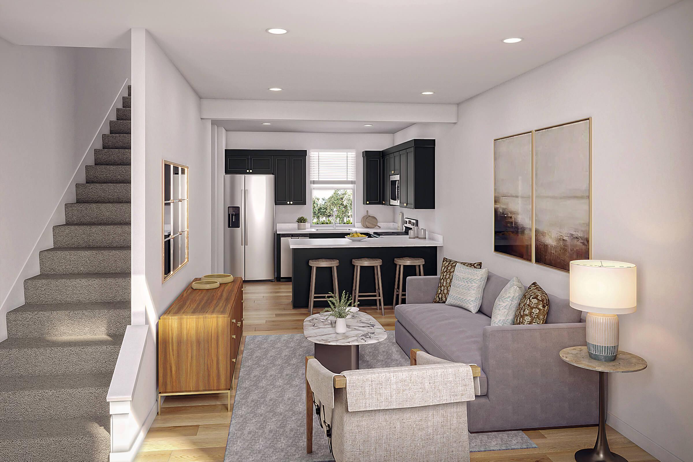 A modern living space featuring a cozy seating area with a gray sofa, a pair of stylish armchairs, and a coffee table. The room has a staircase leading to another level, a contemporary kitchen with dark cabinetry, a refrigerator, and bar stools at the counter. Natural light filters in through a window.