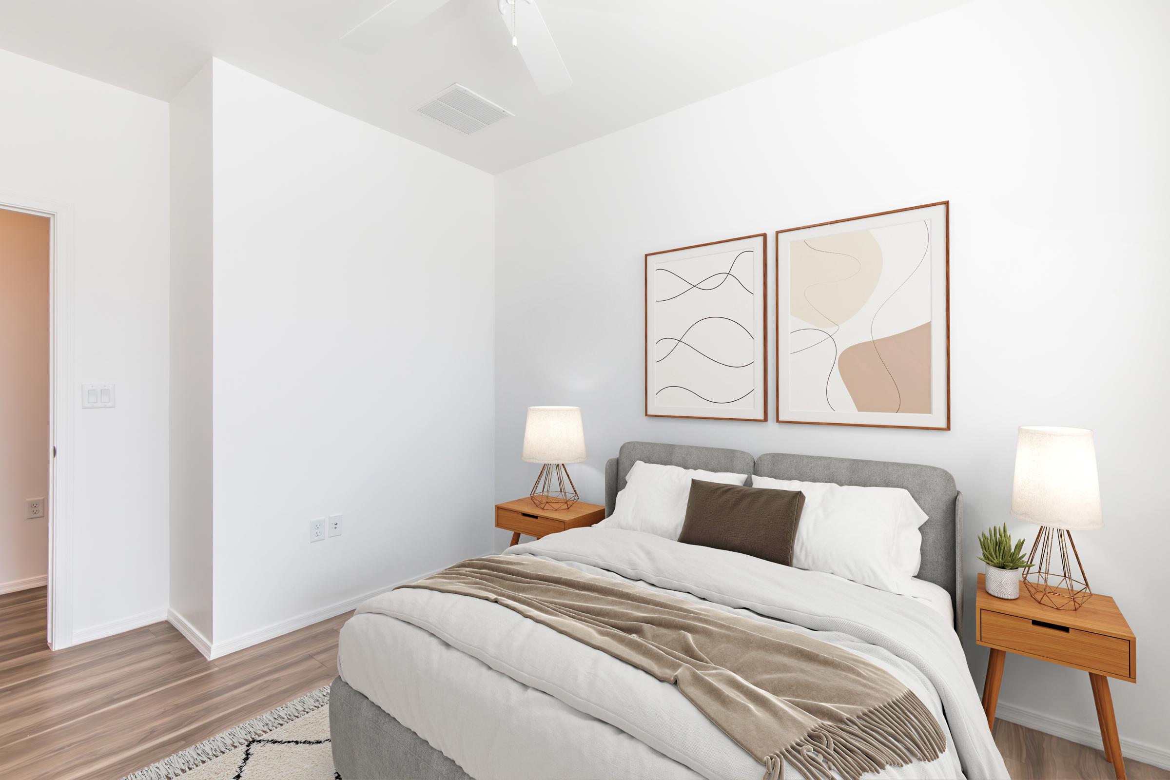 A cozy bedroom featuring a gray upholstered bed with white and brown bedding, two wooden nightstands with lamps, and abstract wall art. The room has neutral walls and hardwood flooring, creating a calm and inviting atmosphere. A small plant adds a touch of greenery.