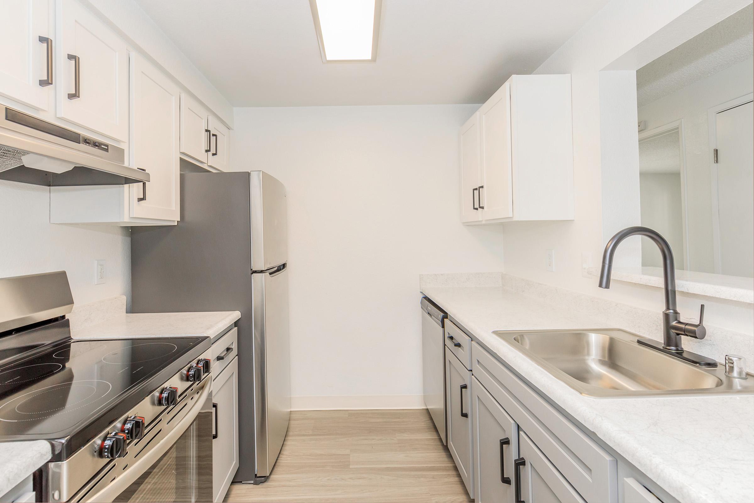Modern kitchen featuring stainless steel appliances, including a refrigerator, oven, and range. Light-colored cabinets provide storage, and a single-basin sink is installed in a countertop with a marble-like finish. The space is well-lit with a ceiling light and has a clean, contemporary aesthetic.