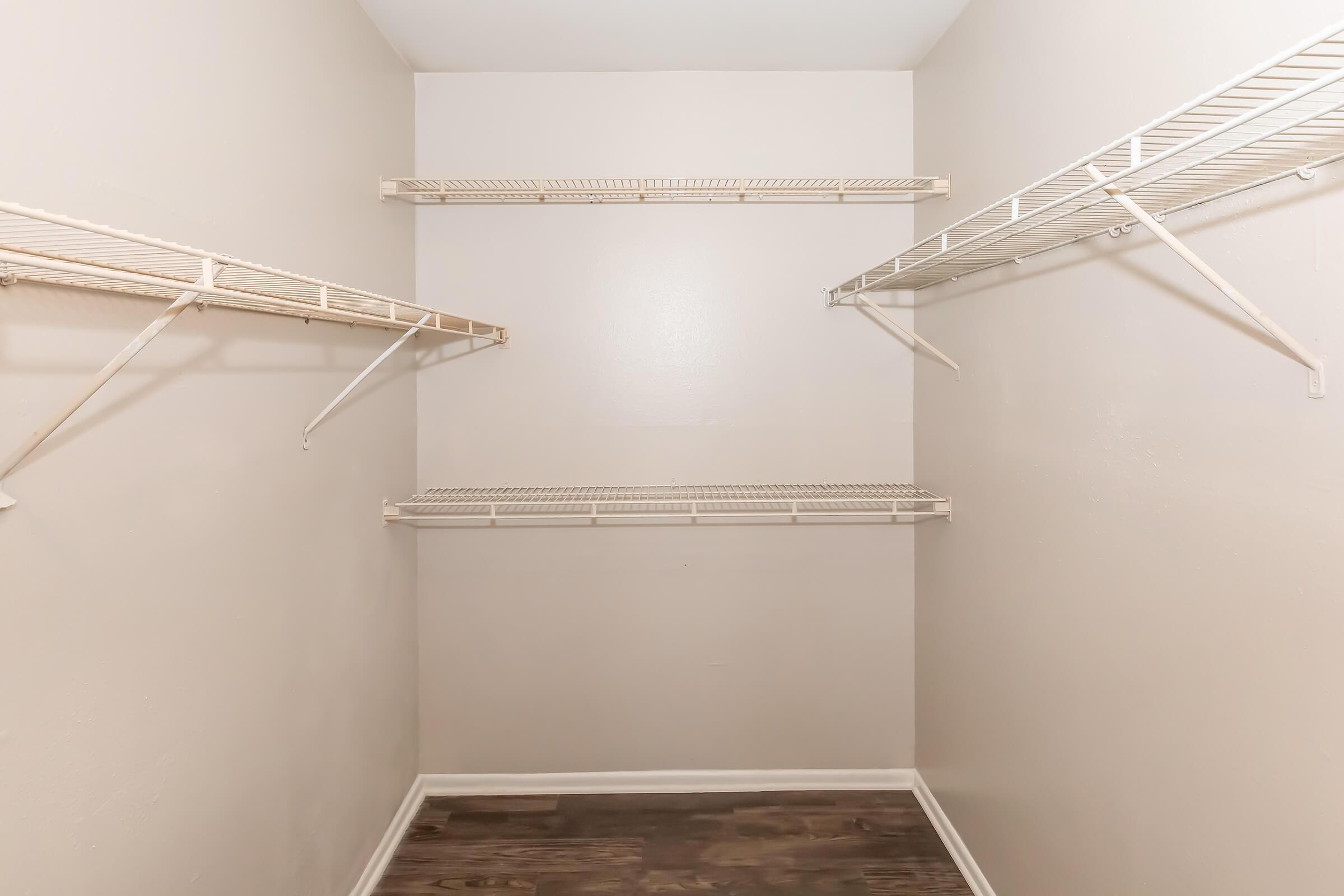 Empty closet with white wire shelving on both side walls, light-colored walls, and a wooden floor. The space is unoccupied, creating a minimalistic appearance.