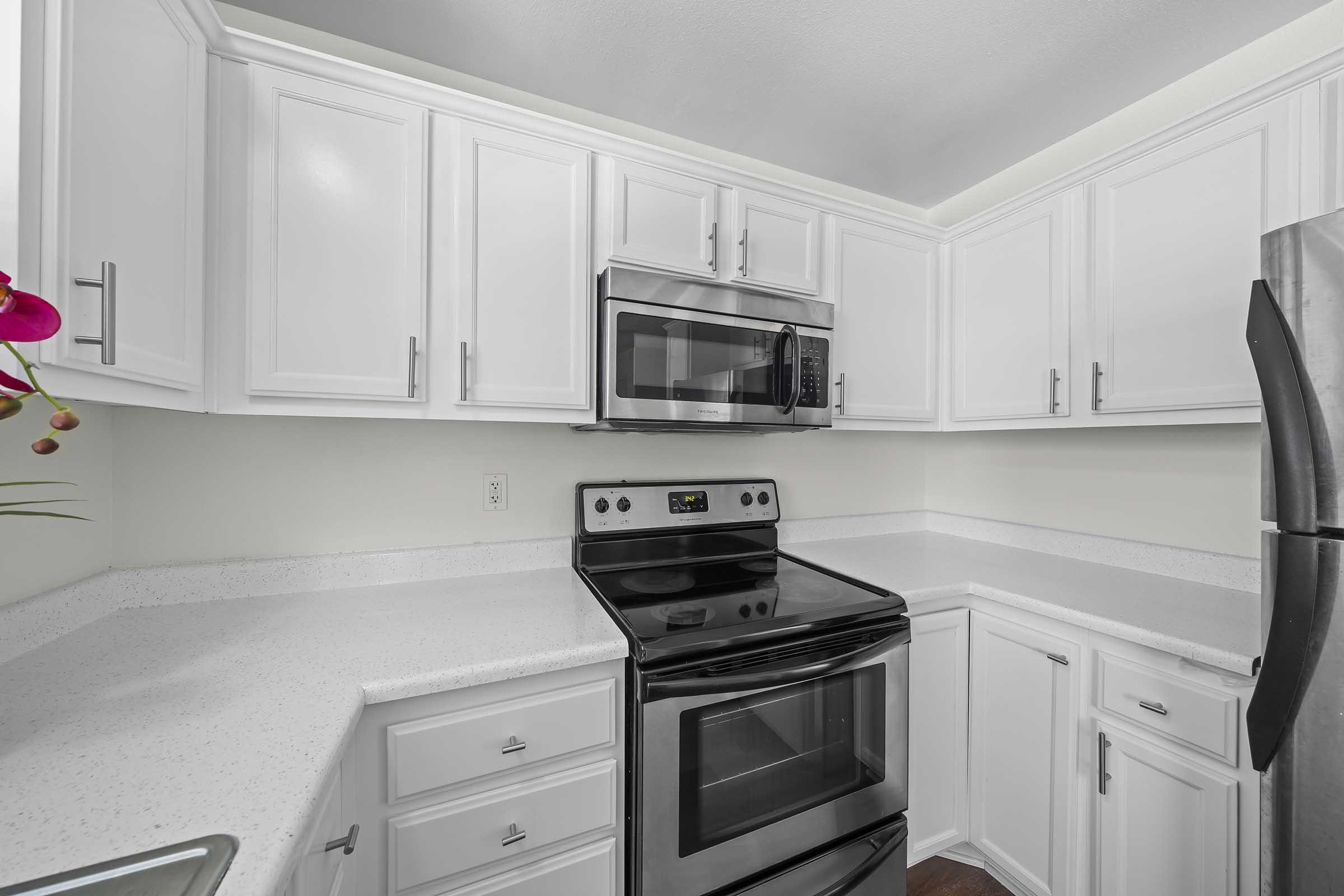 Modern kitchen with white cabinetry, stainless steel appliances including a microwave and an electric stove, and a light-colored countertop. The walls are painted a soft green, adding a fresh touch to the space. A small plant is visible on the counter, enhancing the inviting atmosphere.
