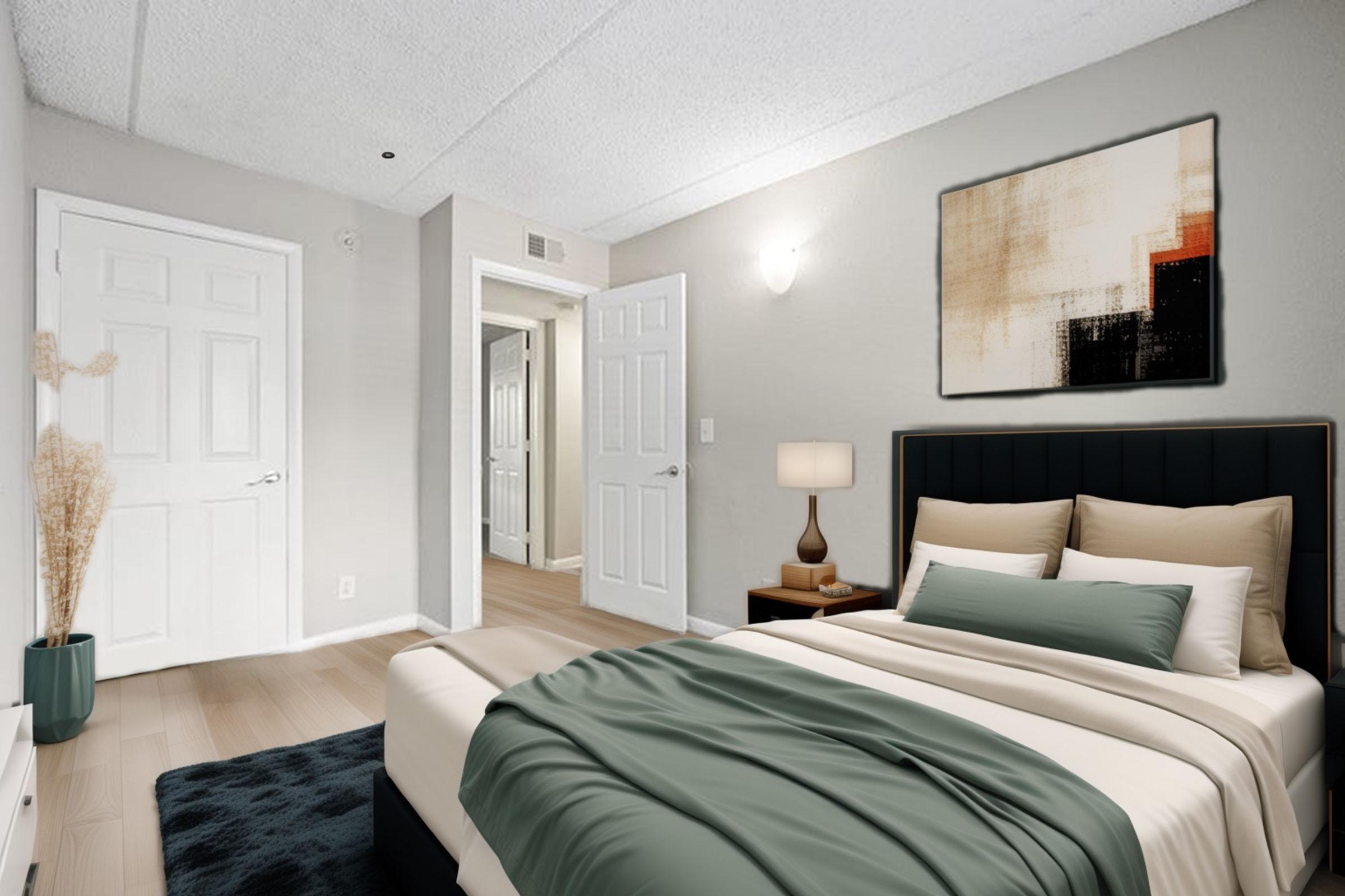 A modern bedroom featuring a bed with beige and green bedding, a bedside lamp, and an abstract painting on the wall. The room has light gray walls, a closet with double doors, and a wooden floor. Natural light illuminates the space, creating a warm and inviting atmosphere.