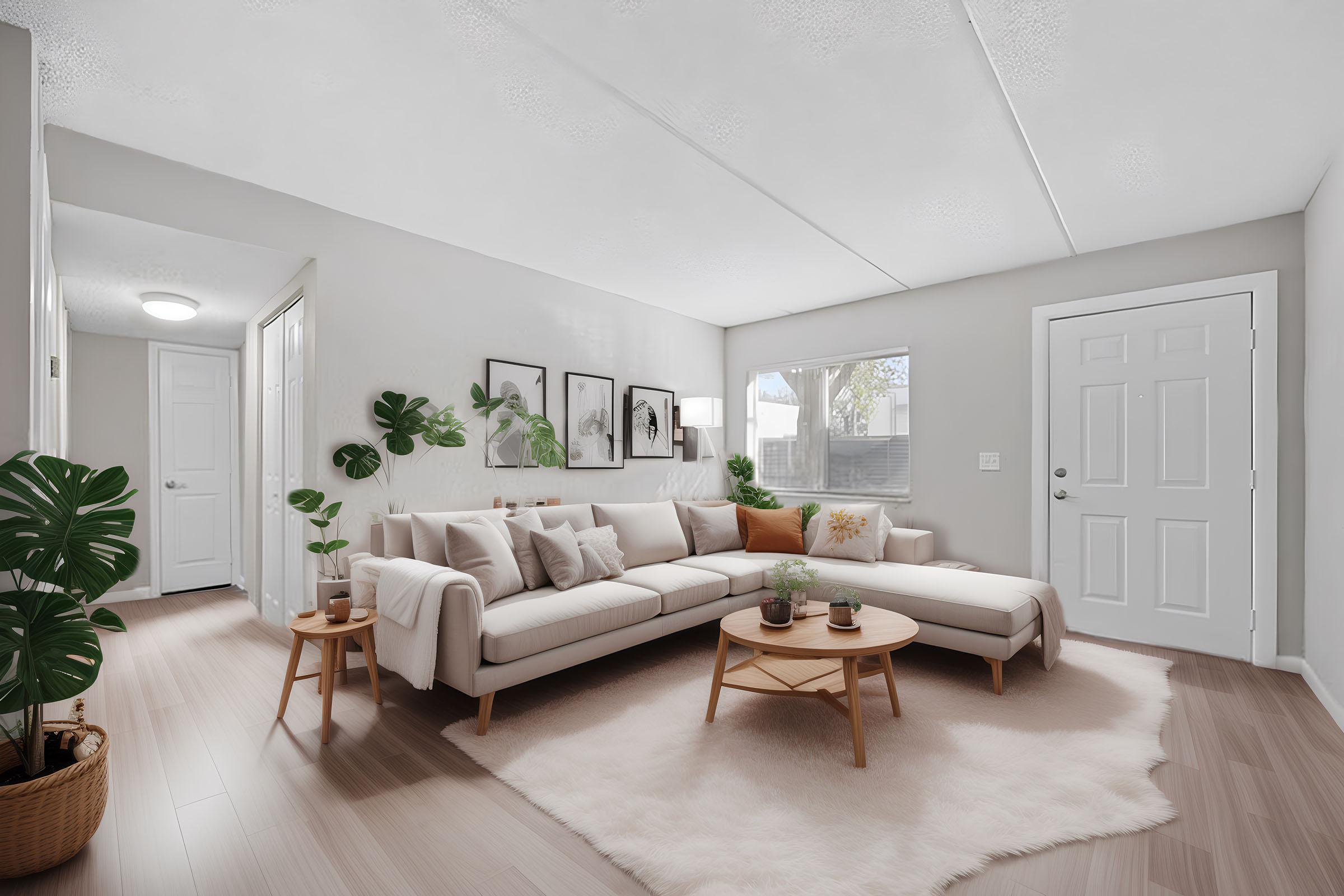 A modern living room featuring a light-colored sectional sofa, a wooden coffee table, and a plush area rug. Decorated with indoor plants and framed wall art, the room has large windows allowing natural light, and a doorway leading to another space. The walls are painted in a soft neutral tone.