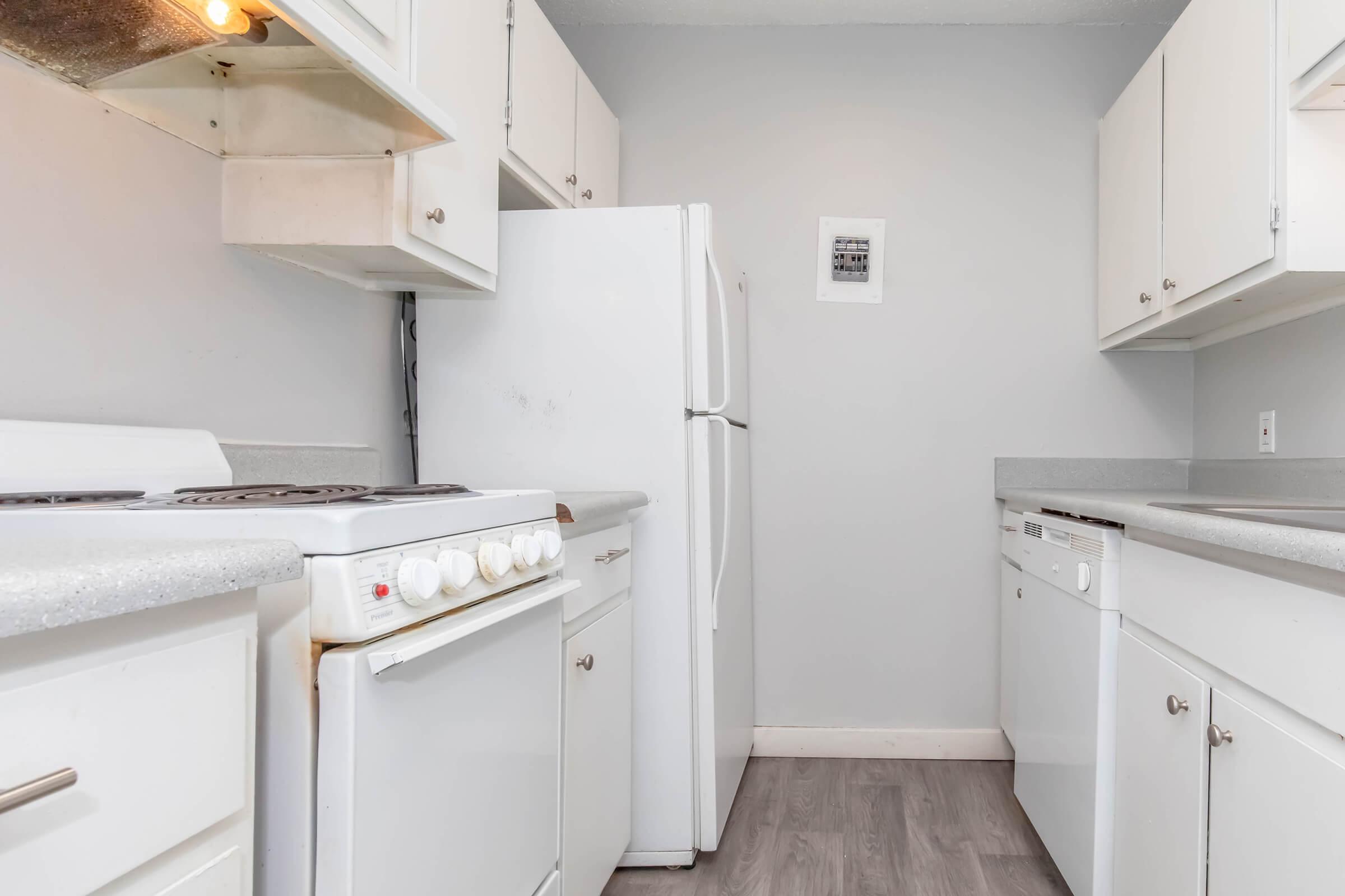 A clean and modern kitchen featuring white appliances, including a stove, refrigerator, and dishwasher. The cabinetry is also white, providing a bright and airy feel, while light gray walls enhance the contemporary aesthetic. A framed picture is visible on the wall, adding a touch of decor.