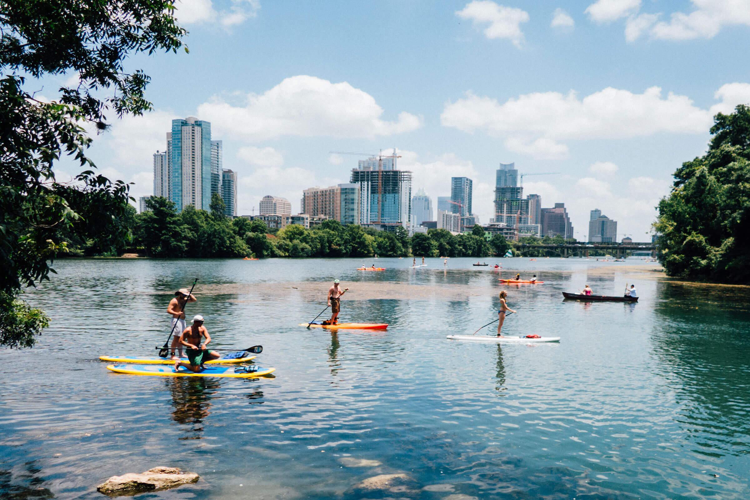 a group of people riding on the back of a boat in the water with Chapultepec in the background