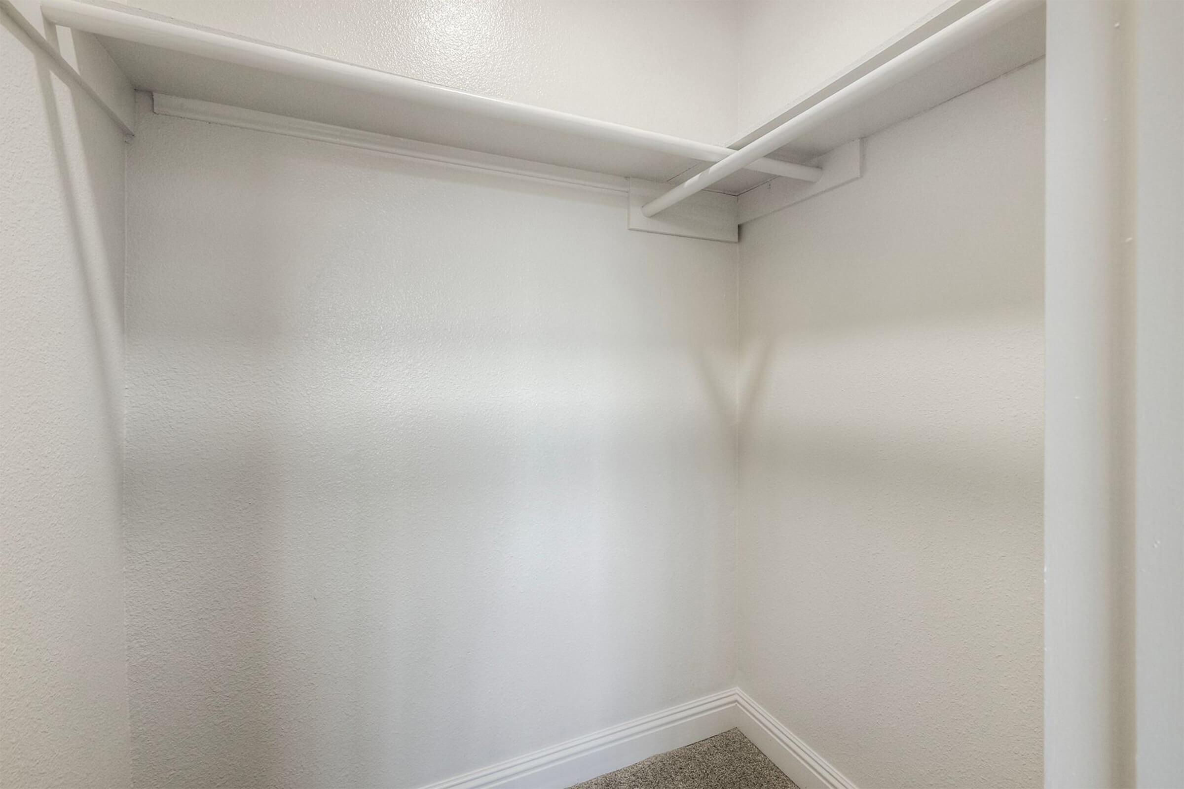 Empty closet with white walls and a single shelf. The floor is covered with light carpet, and there are no items or furnishings present. The lighting is bright, creating a clean and spacious appearance.