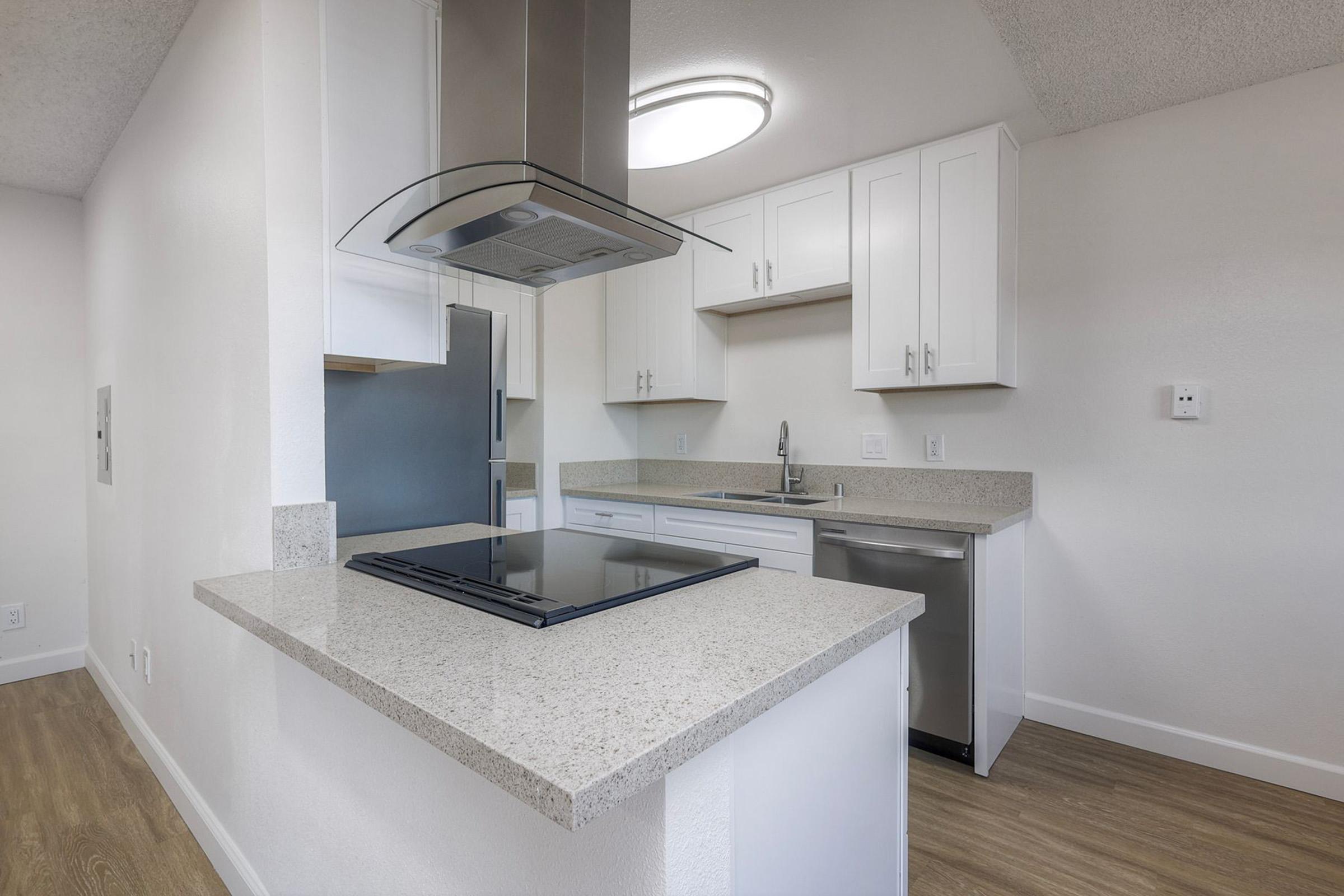 Modern kitchen featuring white cabinetry, a stainless steel refrigerator, and a sleek stovetop integrated into the countertop. There is a spacious sink and a dishwasher, with light wood flooring and neutral-colored walls creating a bright and inviting atmosphere.