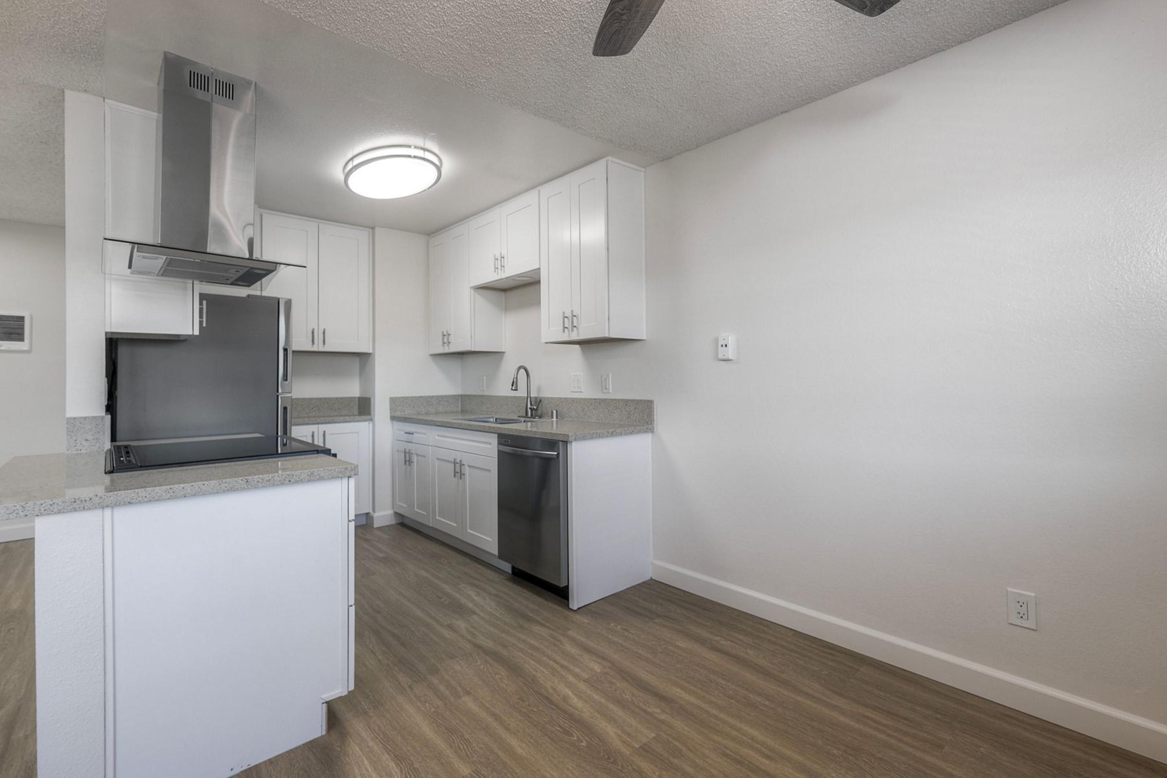 Modern kitchen featuring white cabinetry, stainless steel appliances, a gray countertop, and a large circular ceiling light. The open layout includes a kitchen island and hardwood flooring, creating a bright and inviting space.