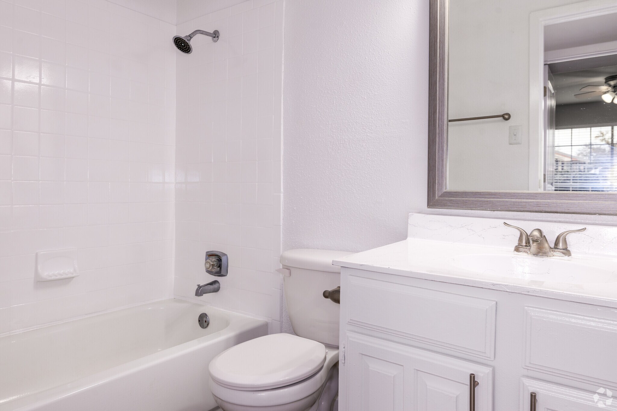 A clean bathroom featuring a white tiled shower with a bathtub, a toilet, and a modern vanity with a mirror. Natural light is visible through a window, enhancing the spacious feel of the room.