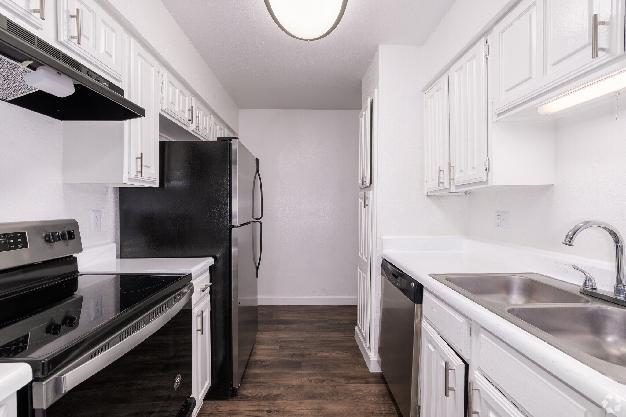 Modern kitchen featuring white cabinetry, a black refrigerator, a stainless steel dishwasher, and a black stove. The space includes a double sink and laminate flooring, creating a clean and inviting atmosphere.