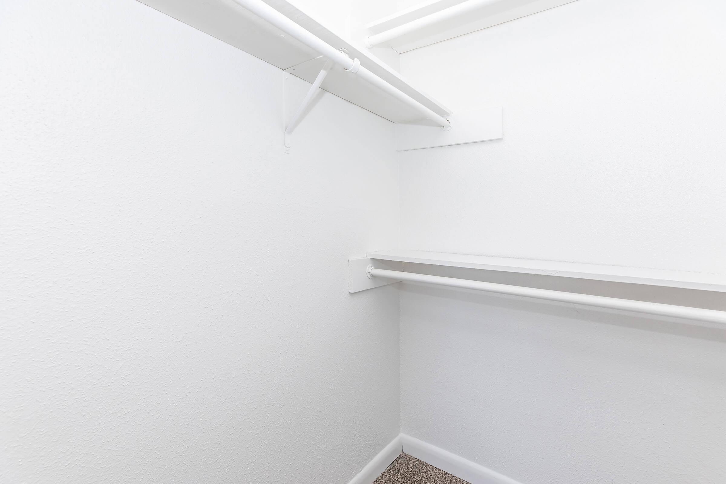 Empty closet space with white walls and shelving. The closet features two horizontal rods for hanging clothes and a carpeted floor, creating a minimalistic and organized appearance.