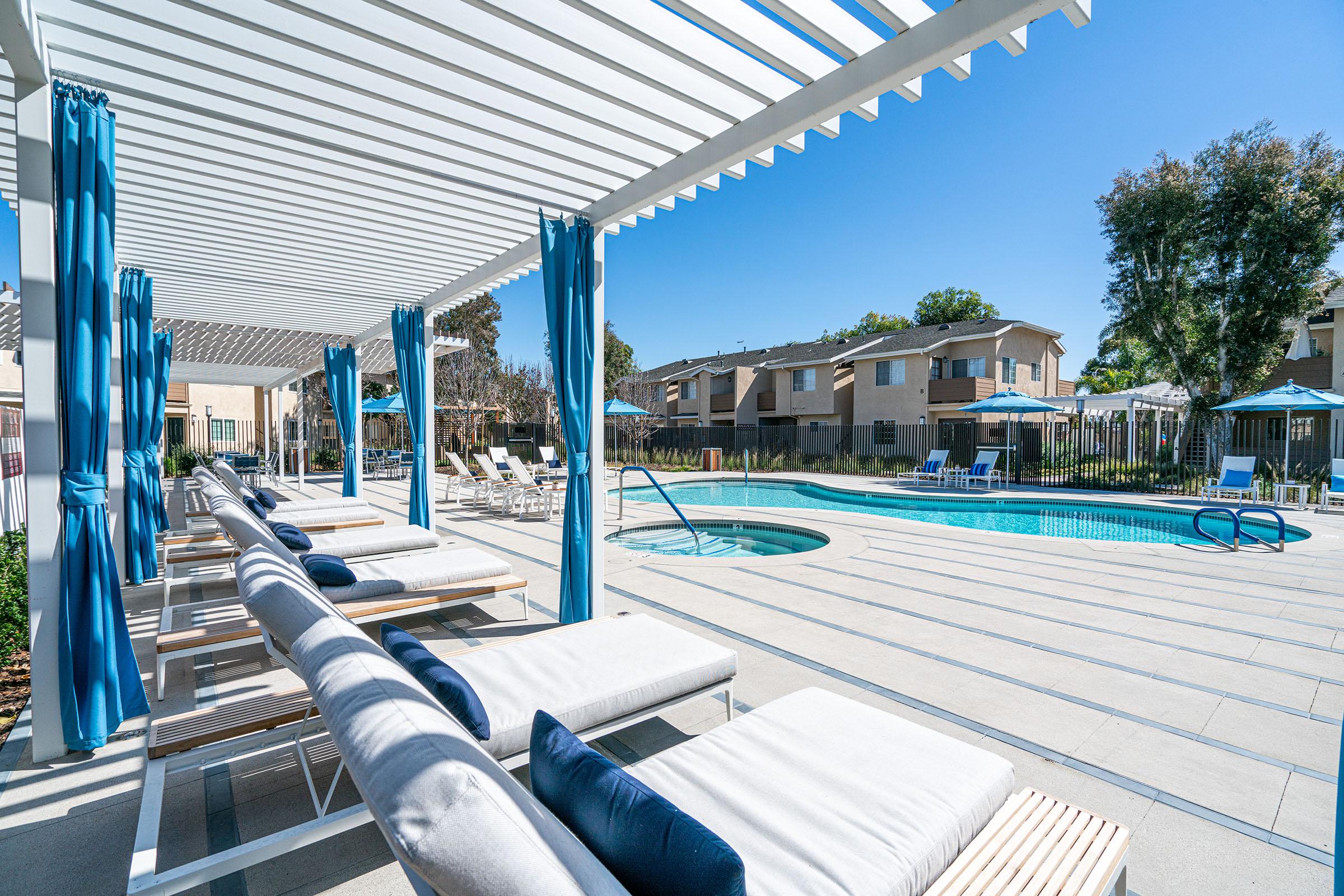 white lounge chairs under a pergola next to the community pool