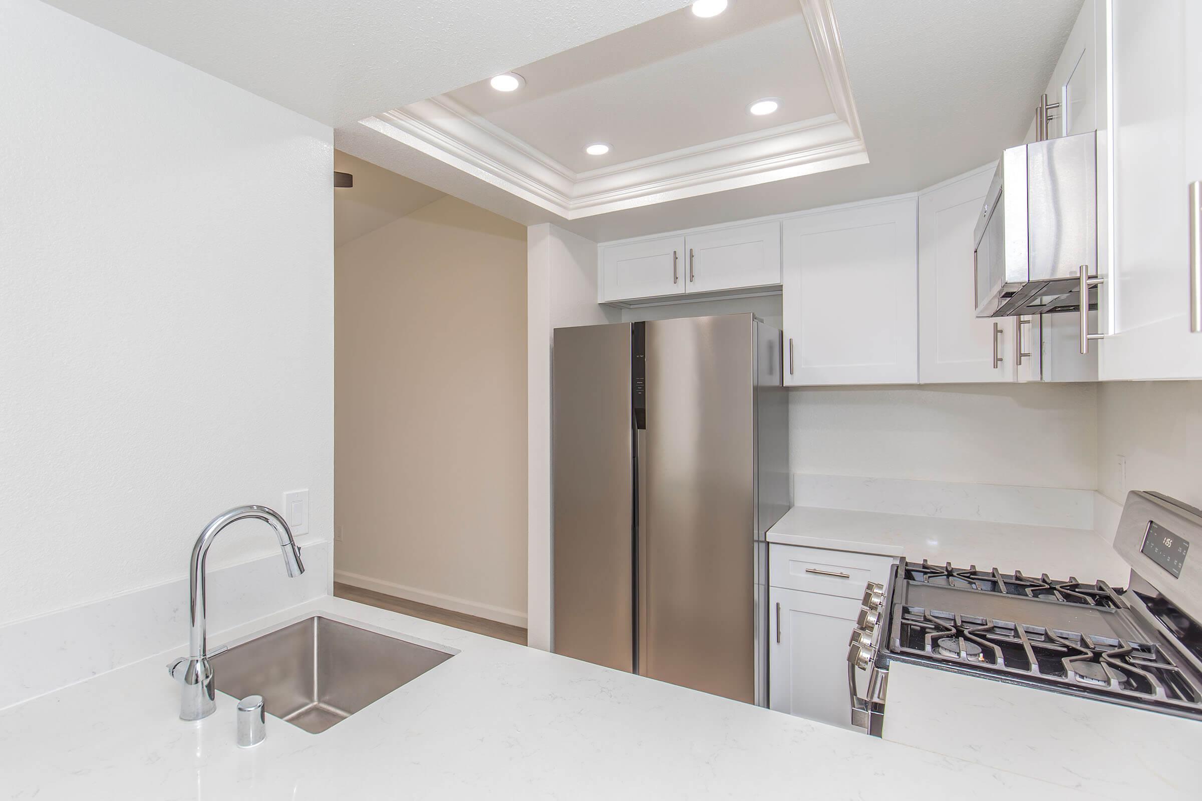 Modern kitchen featuring white cabinetry, stainless steel appliances, and a sleek countertop. A large refrigerator is visible next to a gas stove and oven. The space has recessed lighting and a contemporary design, creating a bright and inviting atmosphere.