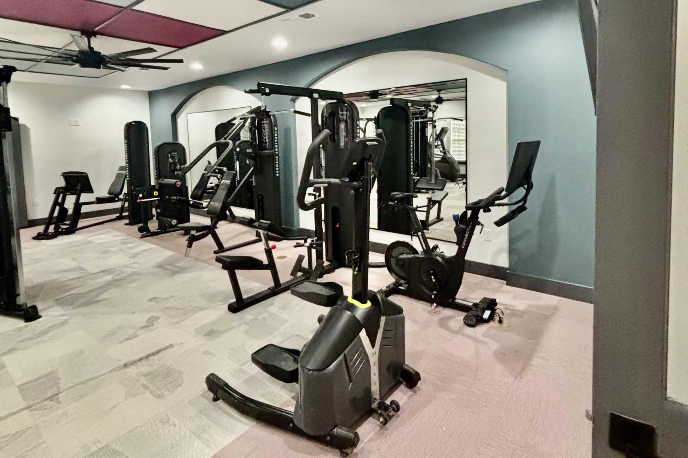 A modern gym interior featuring various exercise equipment including weight machines, a stationary bike, and a mirror on the wall. The space has a neutral color scheme with soft lighting and is neatly organized, providing an inviting atmosphere for workouts.